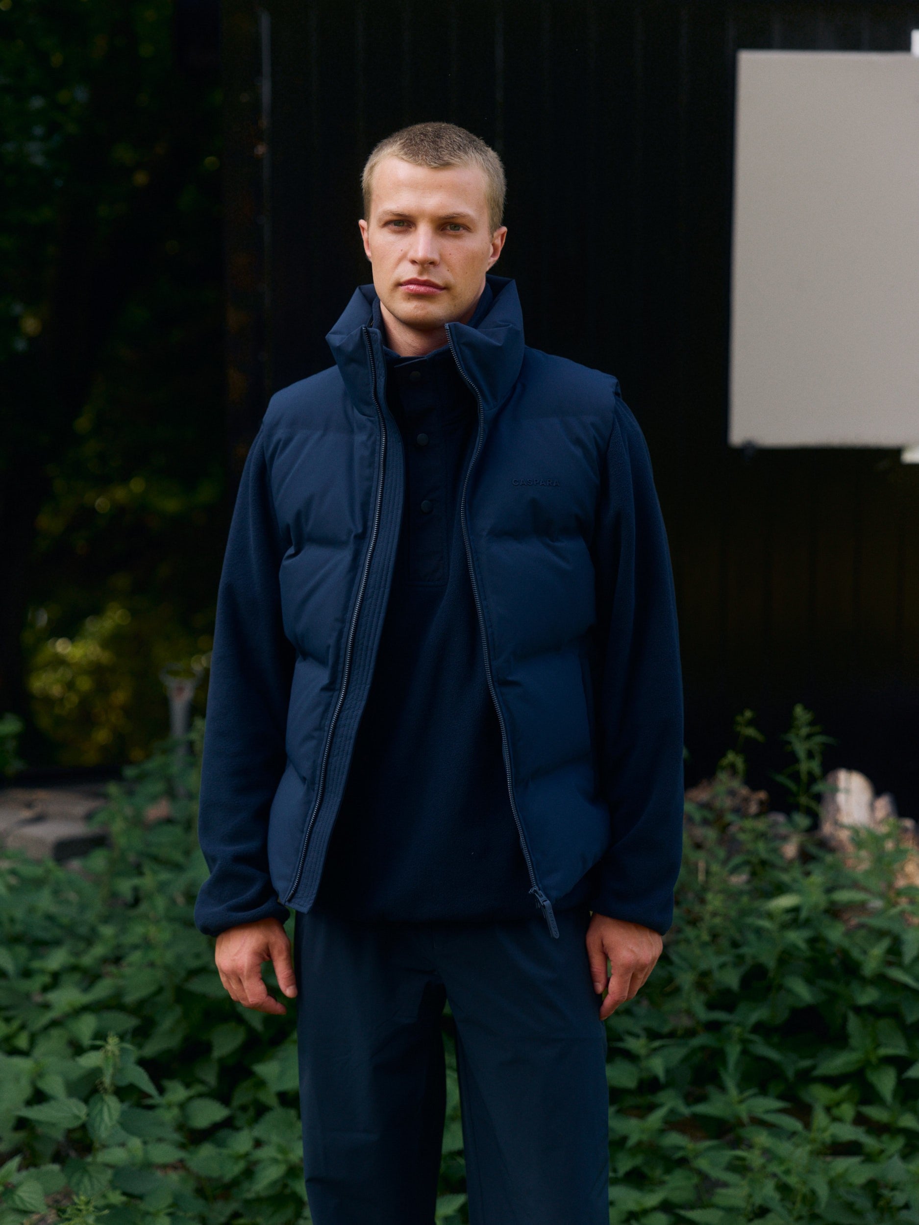 Man wearing a navy polar fleece half-snap pullover under a puffer vest outdoors.