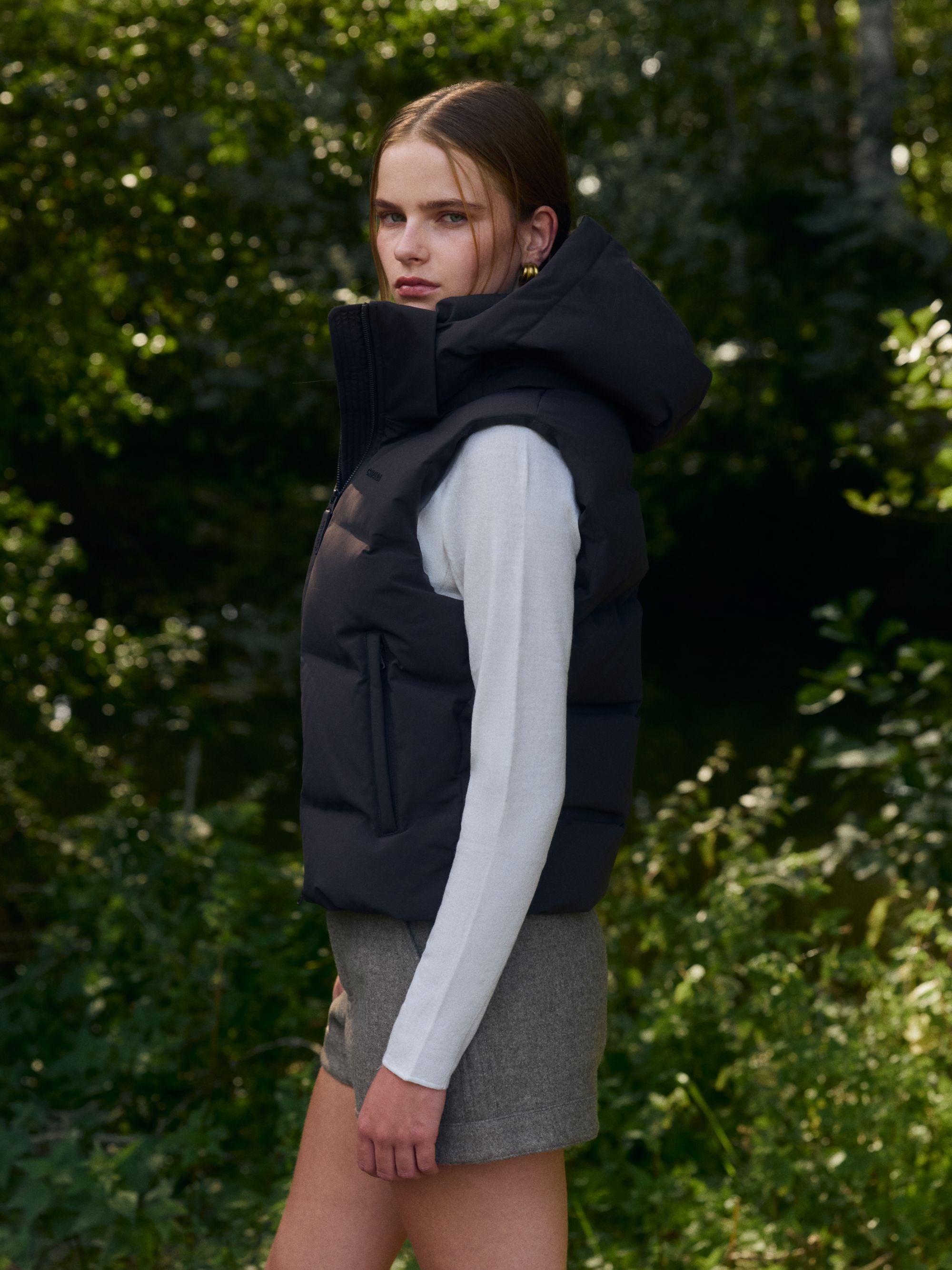 Side view of a woman wearing an espresso CASPARA Aurora puffer vest outdoors.