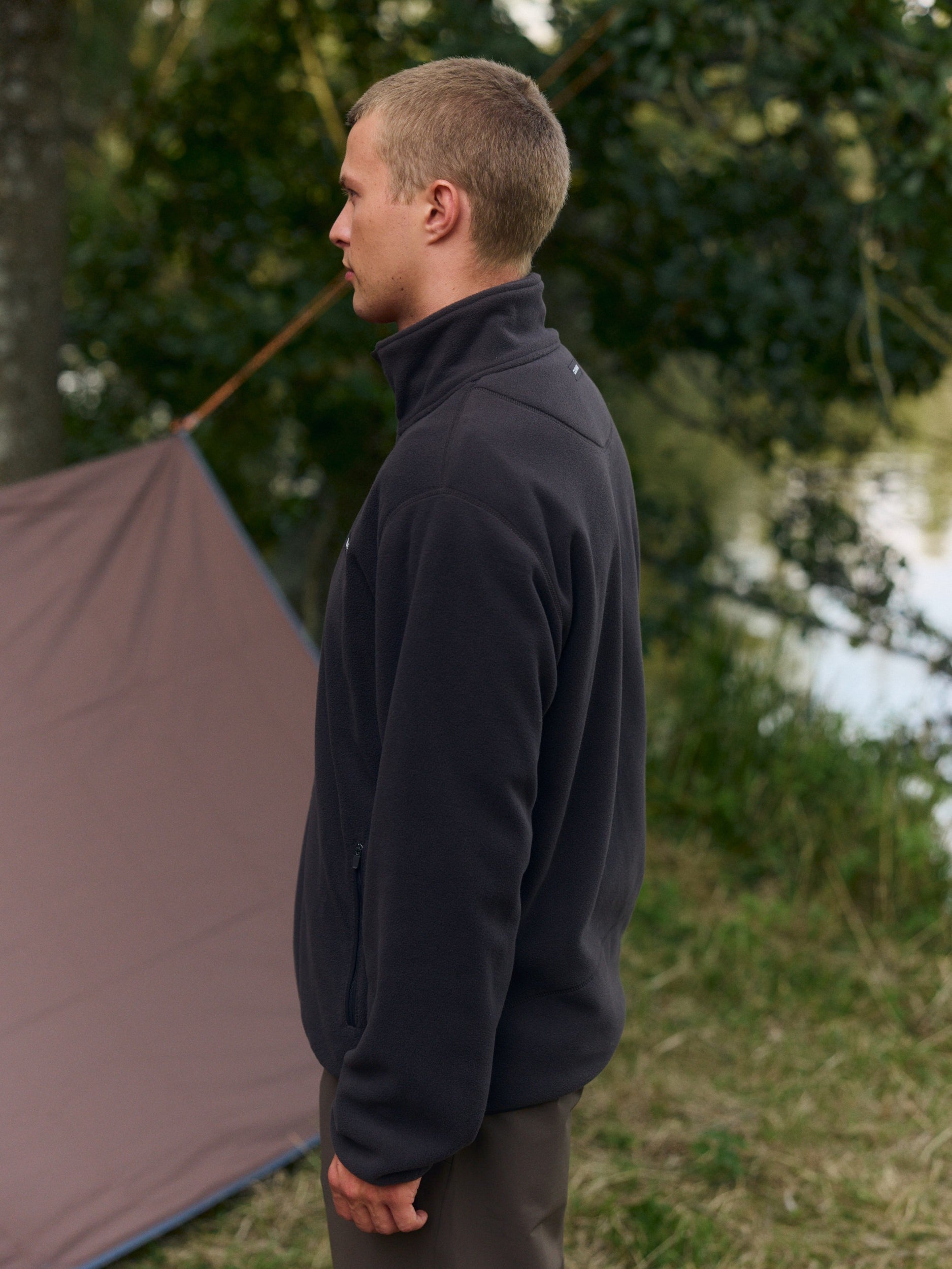 Man wearing a cocoa bean polar fleece pullover outdoors near a camping tent.