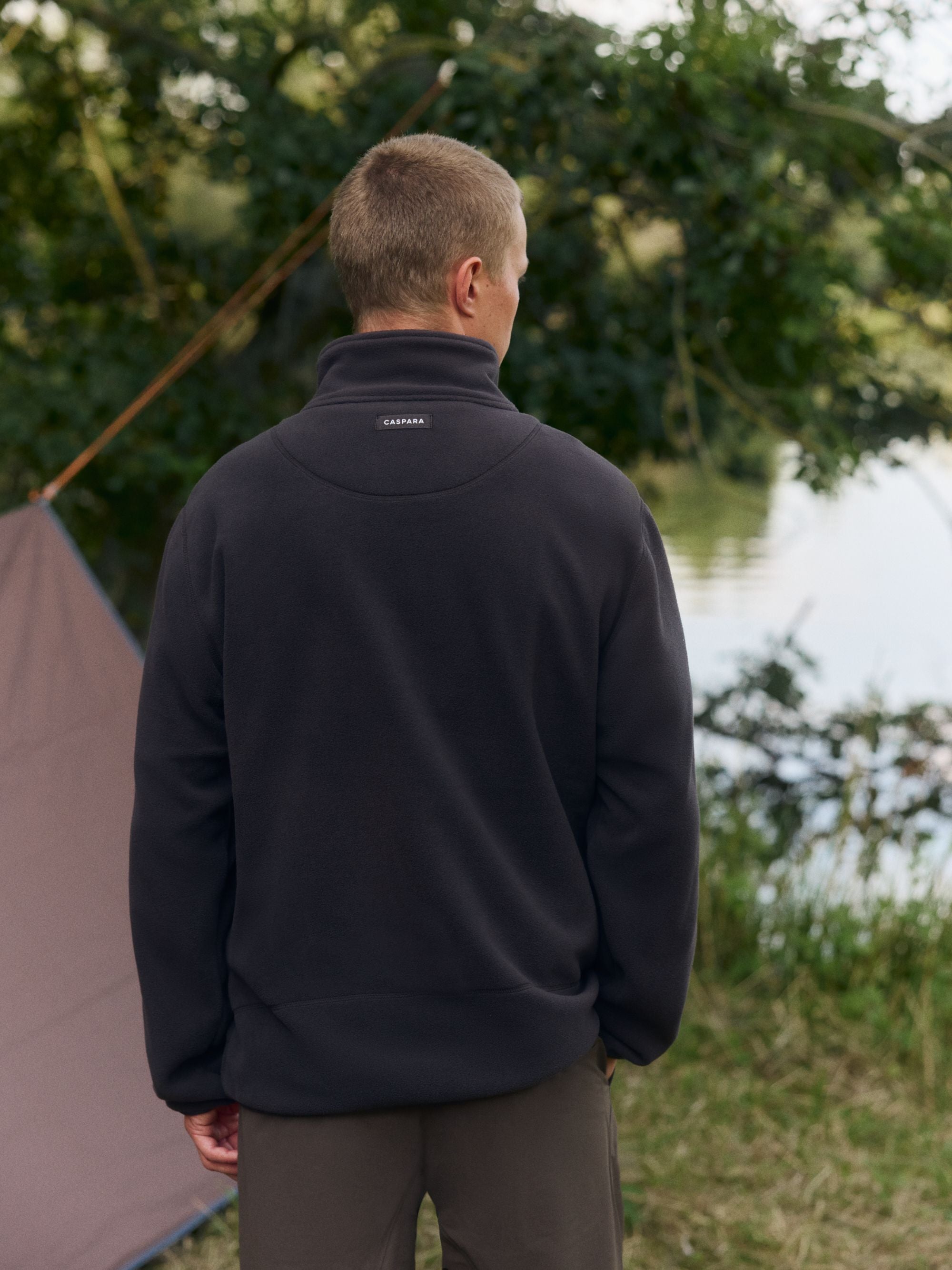 Back view of a man wearing a cocoa bean CASPARA polar fleece pullover outdoors.