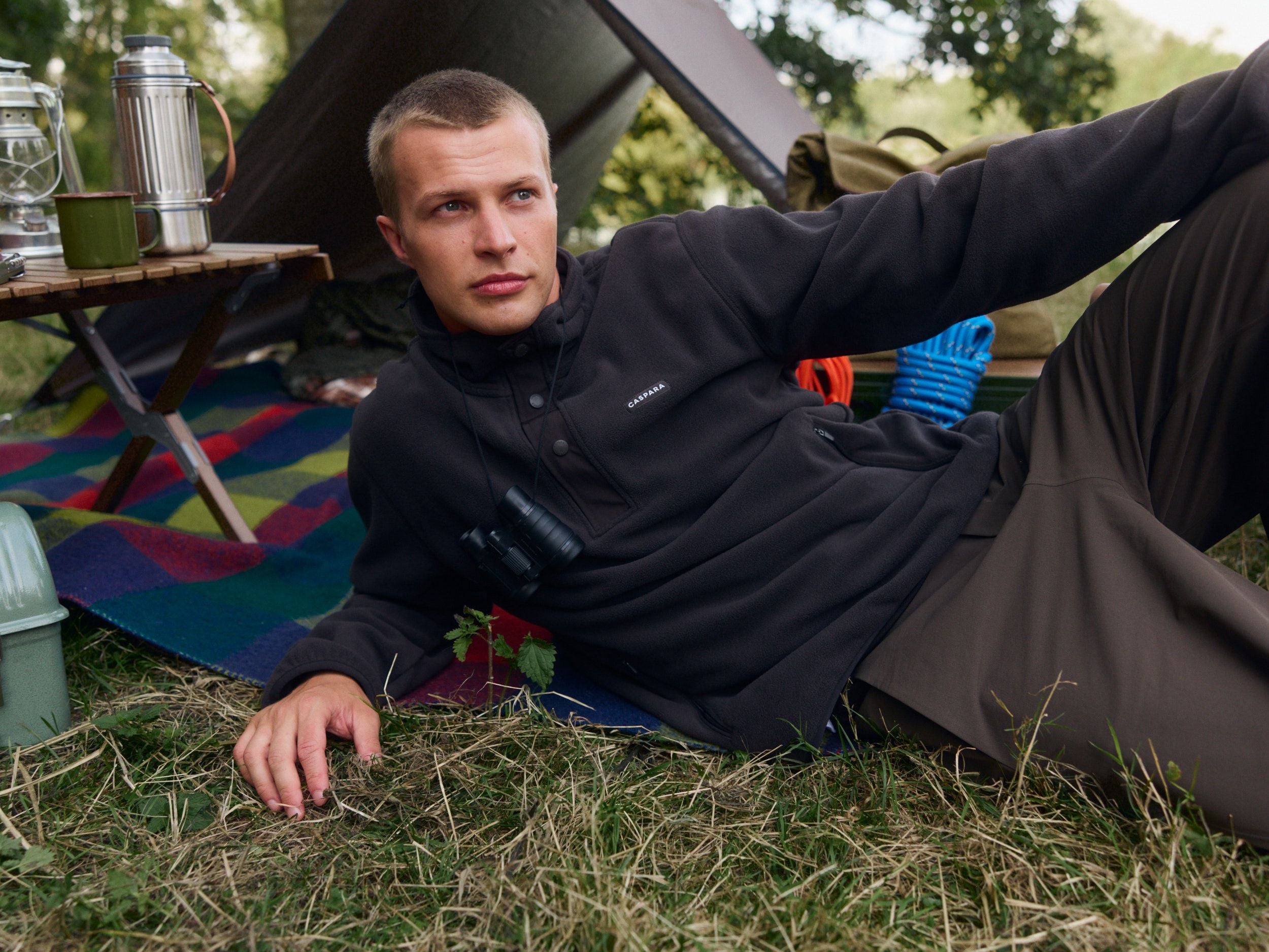 Man wearing a brown polar fleece half-snap pullover relaxing at a campsite.