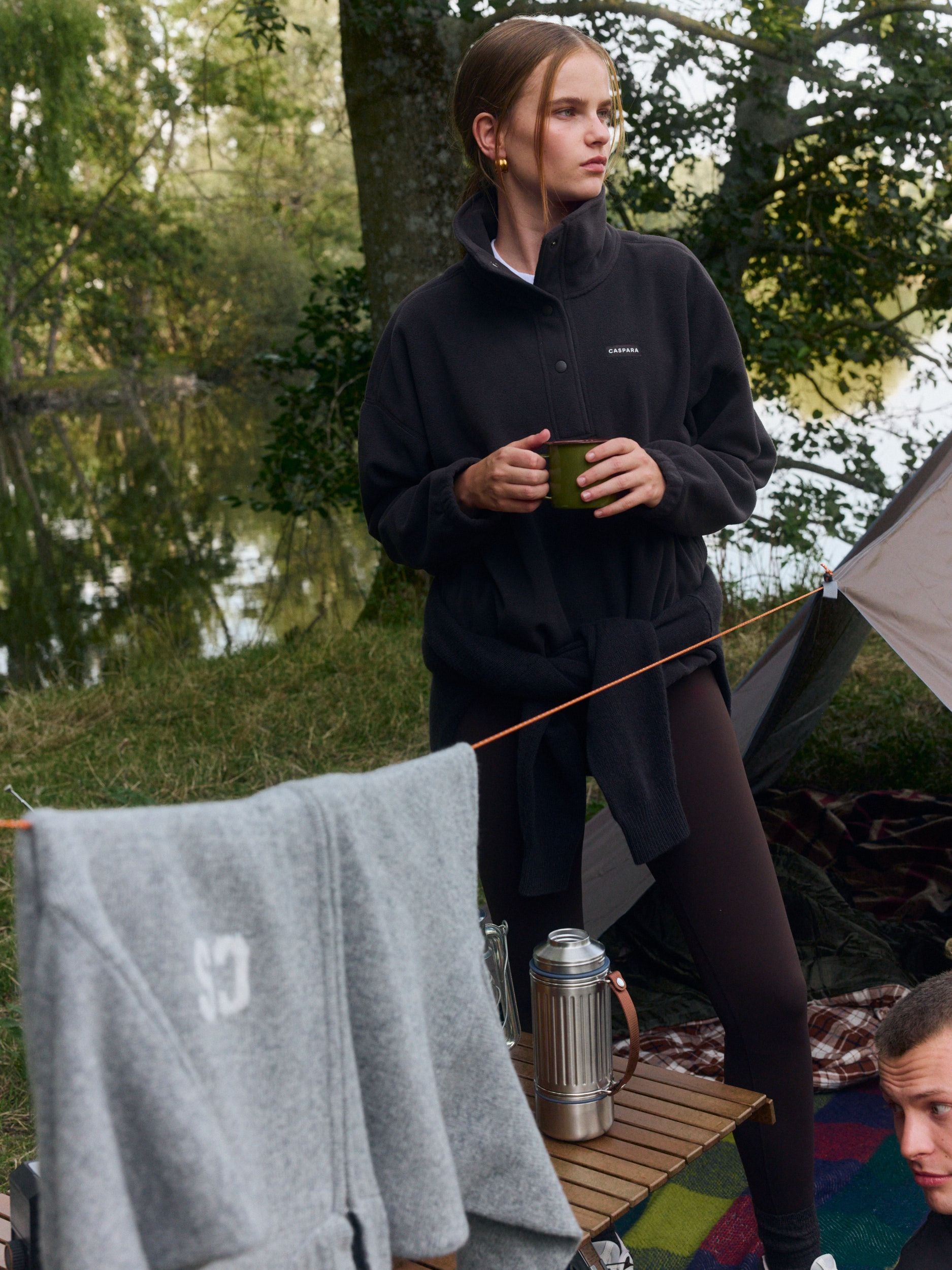 Woman wearing an espresso polar fleece half-snap pullover at a lakeside campsite.