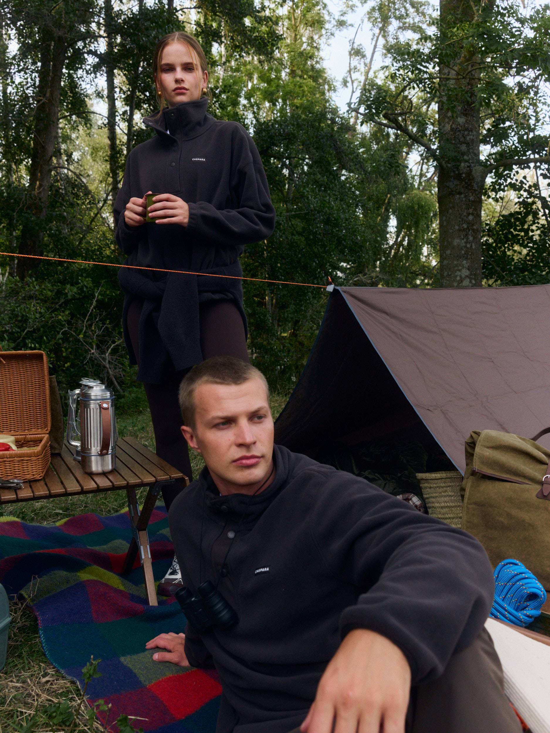 Man and woman wearing espresso polar fleece half-snap pullovers at an outdoor campsite.