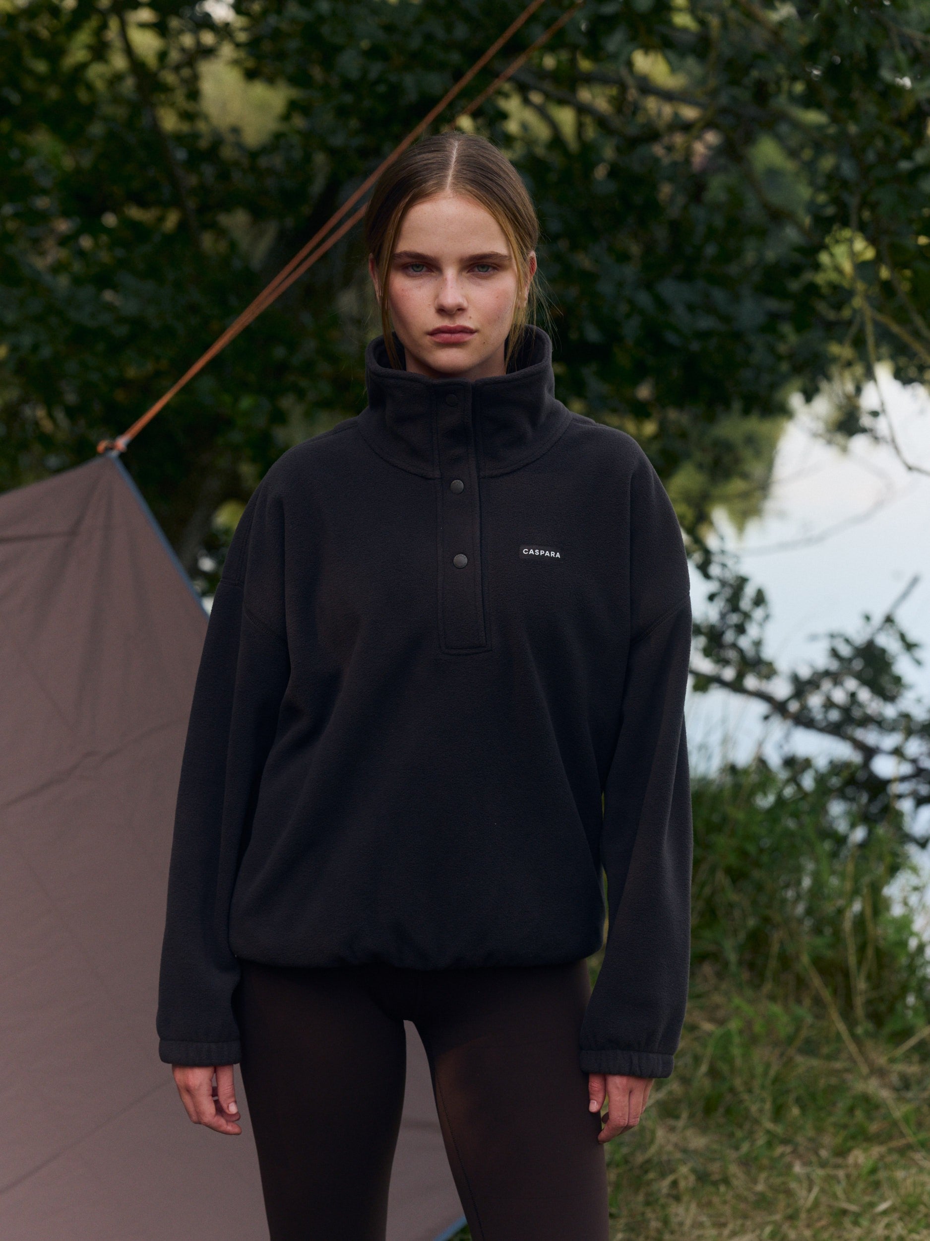 Woman wearing an espresso polar fleece half-snap pullover outdoors near a campsite.