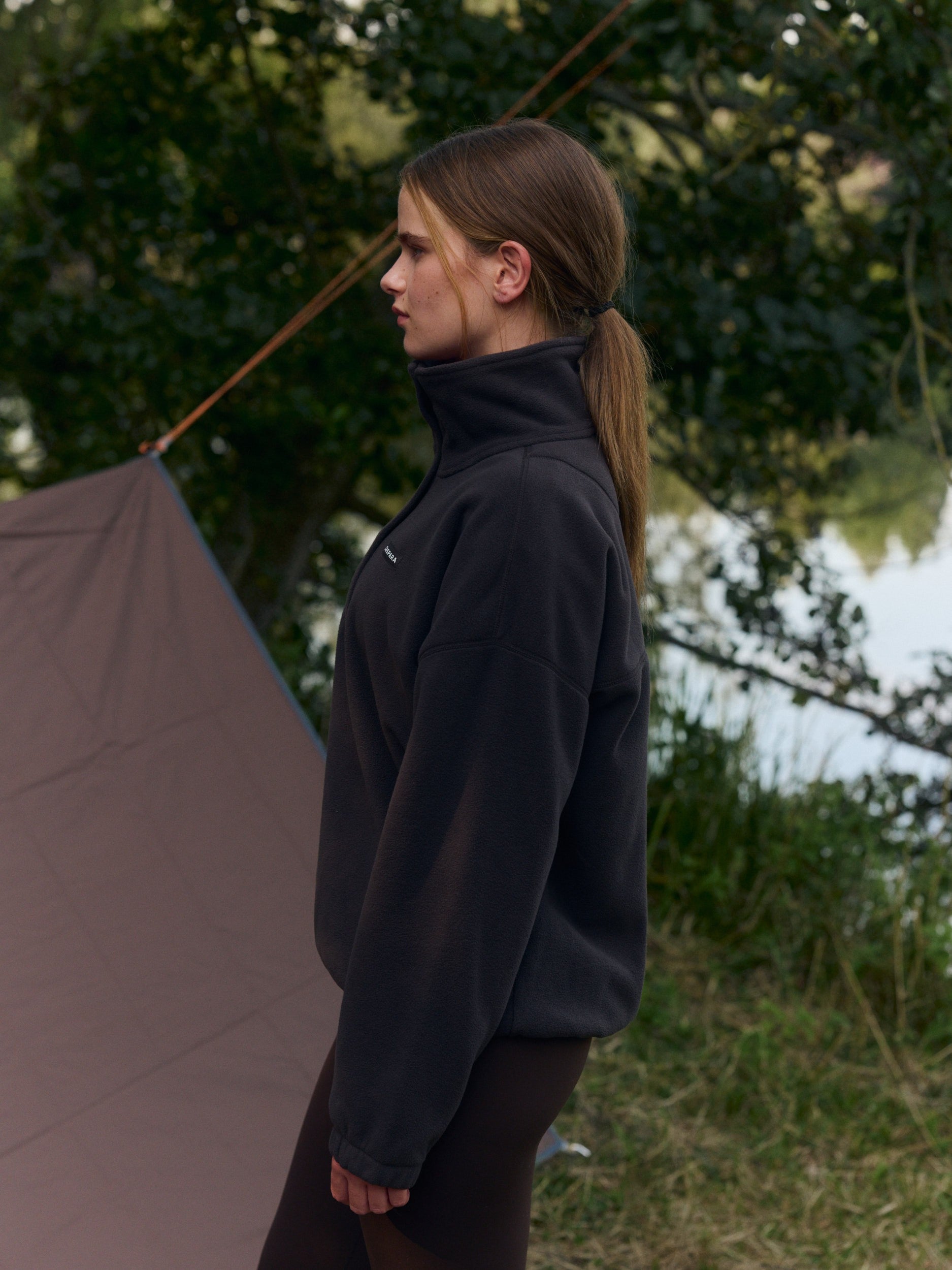 Woman wearing an espresso brown polar fleece half-snap pullover outdoors by a tent.