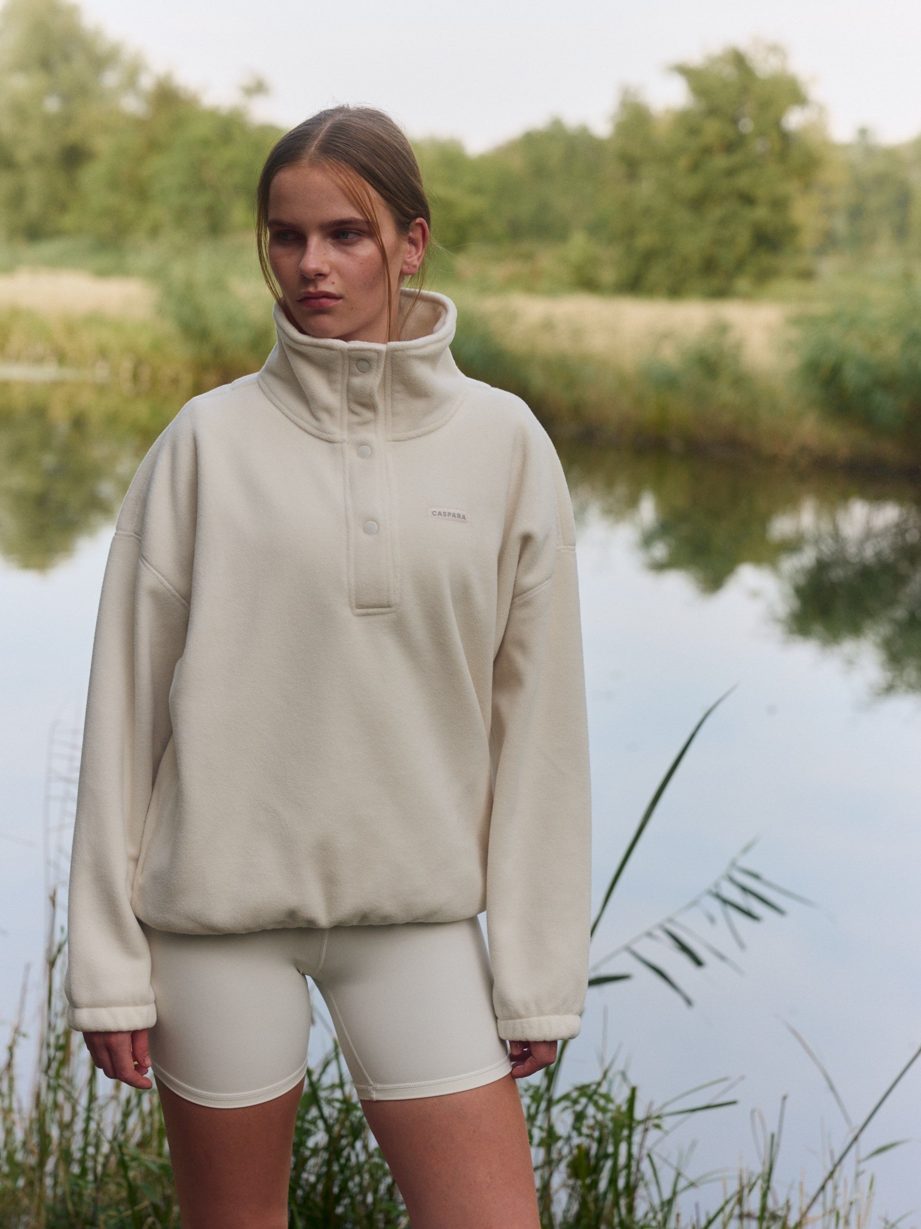 Woman wearing a cream polar fleece half-snap pullover outdoors by a lake.