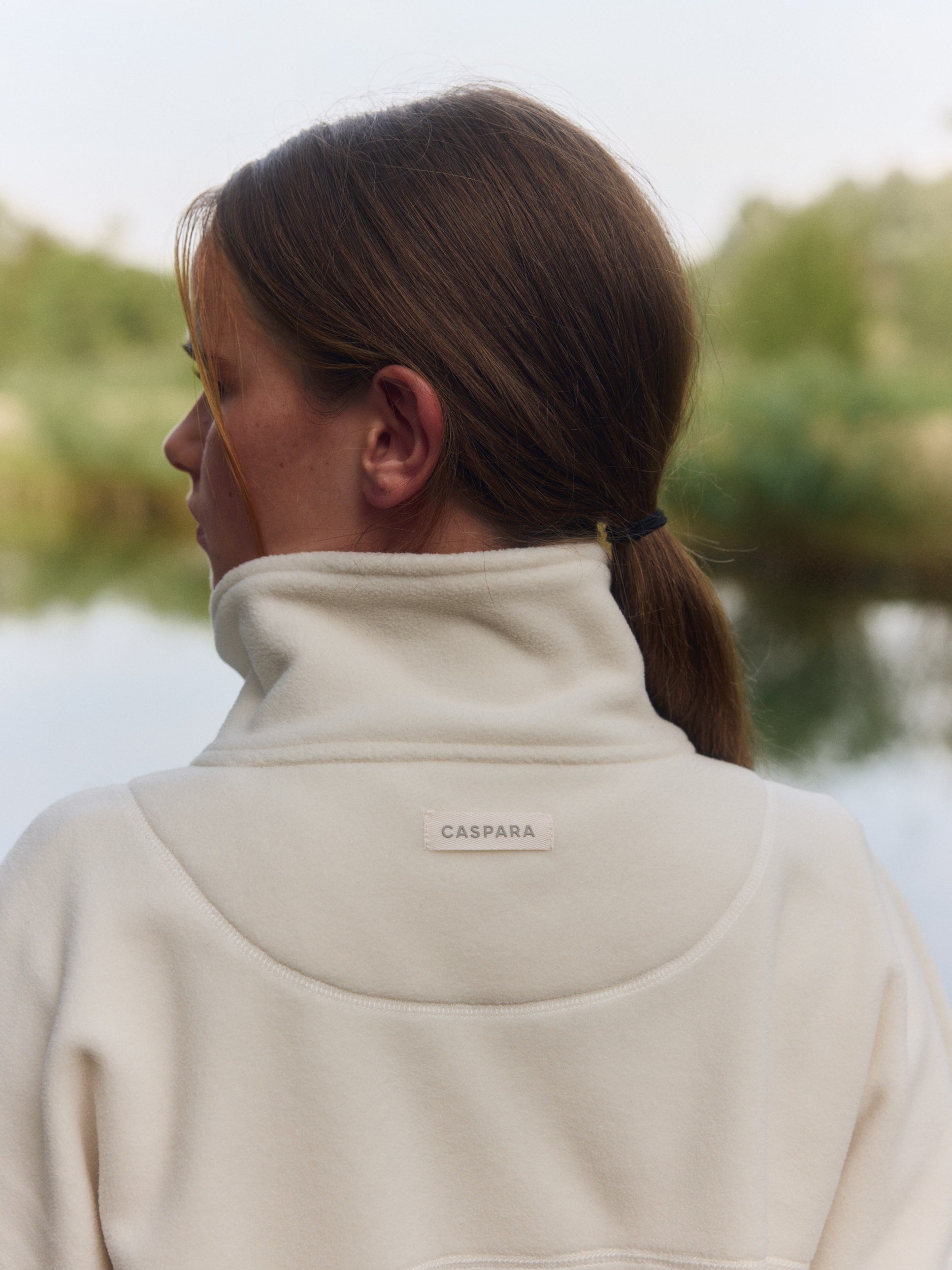Woman wearing a creme polar fleece pullover showing the high collar and CASPARA logo back patch.