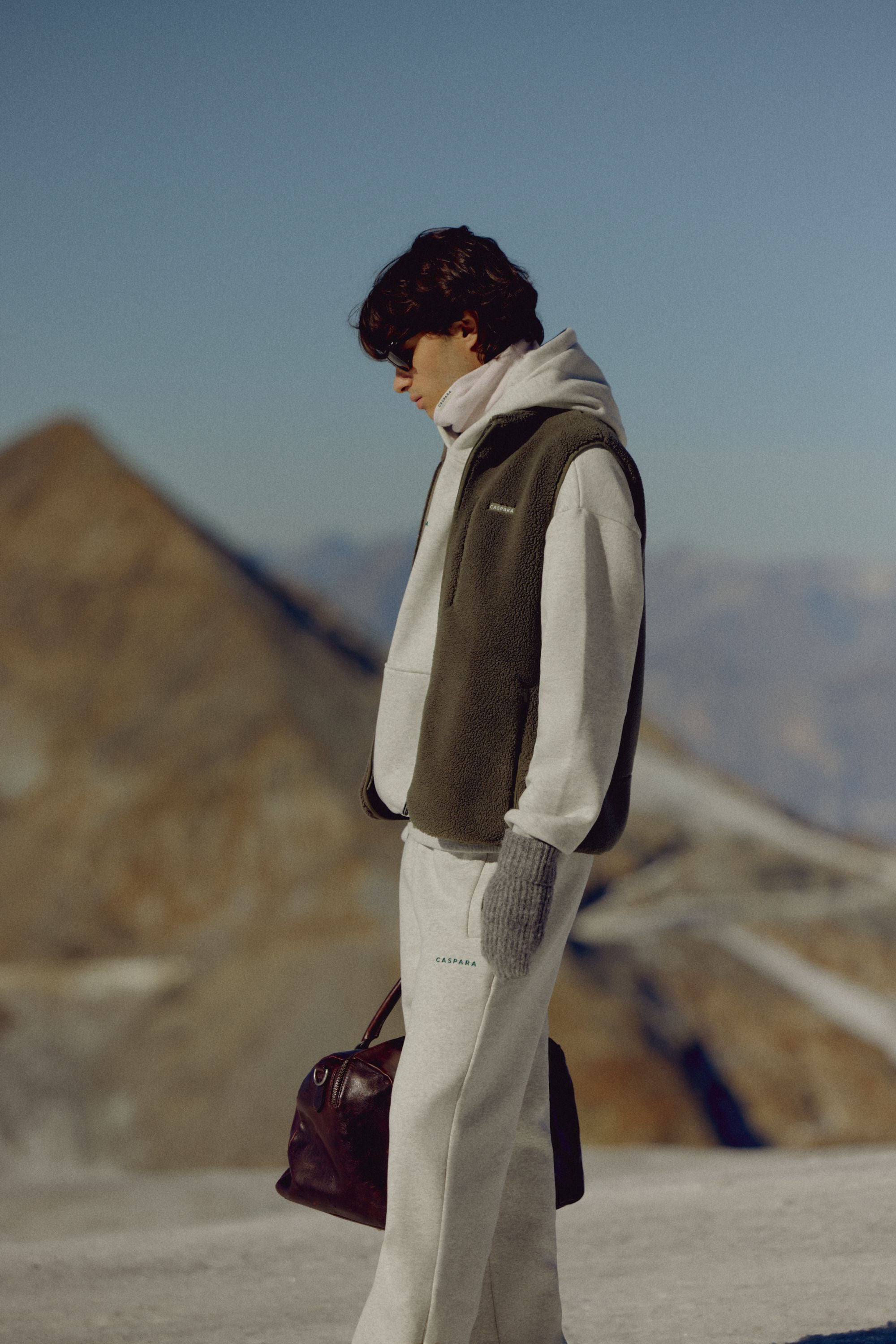 Man wearing a khaki CASPARA Cloudfleece vest standing in a mountain landscape.