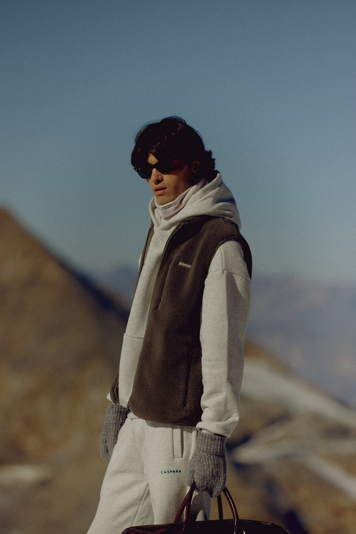 Man wearing a khaki CASPARA Cloudfleece vest outdoors in a mountain landscape.