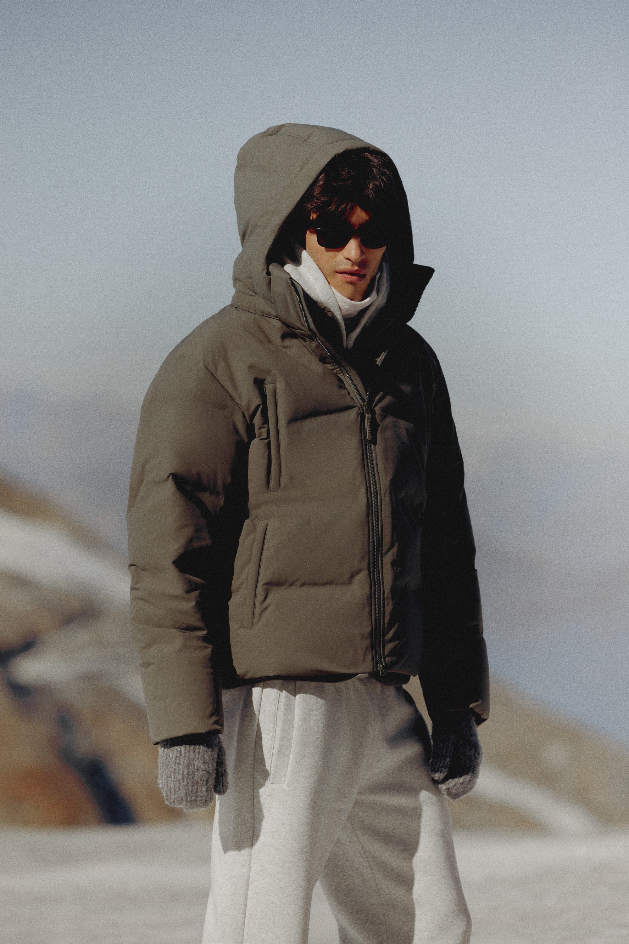 Man wearing a khaki CASPARA Boreal puffer jacket outdoors in a snowy landscape.