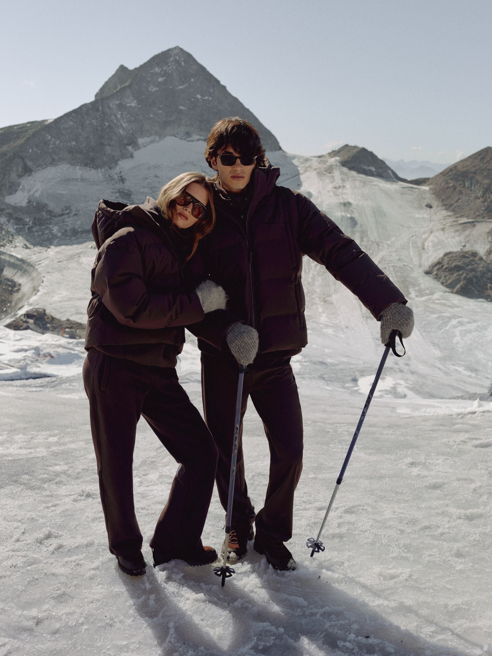 Man and woman wearing cocoa bean CASPARA Aurora puffer jackets on a snowy mountain.