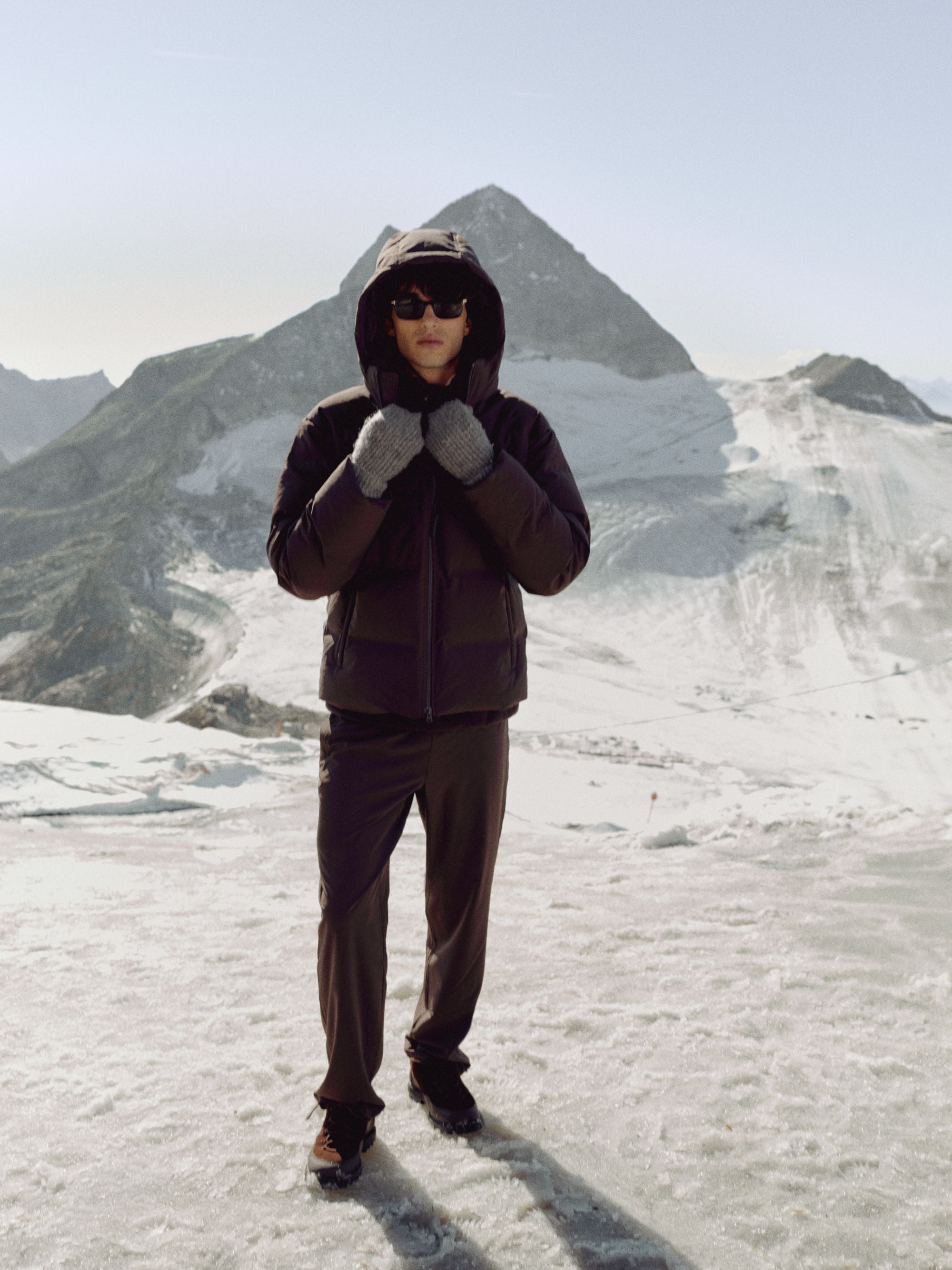 Man wearing a cocoa bean CASPARA Boreal puffer jacket on a snowy mountain.