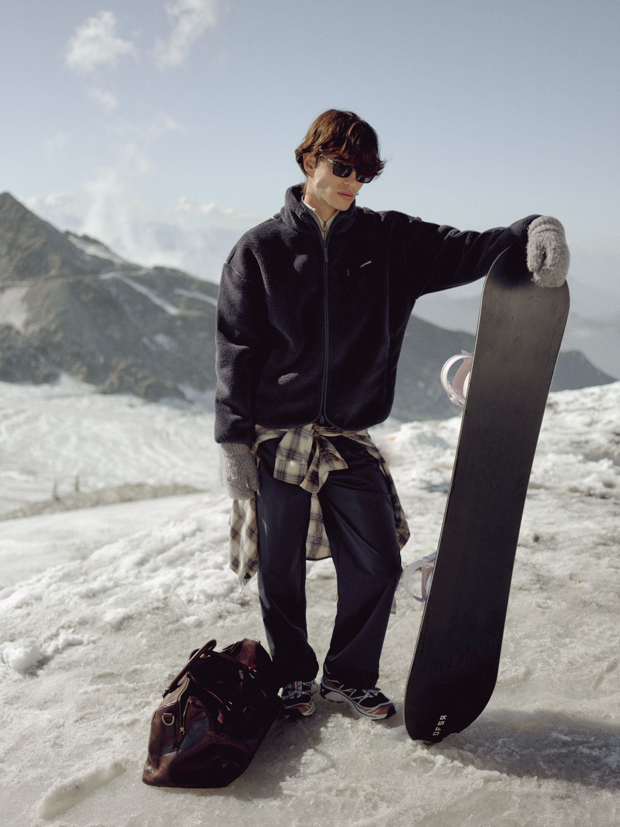 Man wearing a navy CASPARA Cloudfleece jacket holding a snowboard on a snowy mountain.