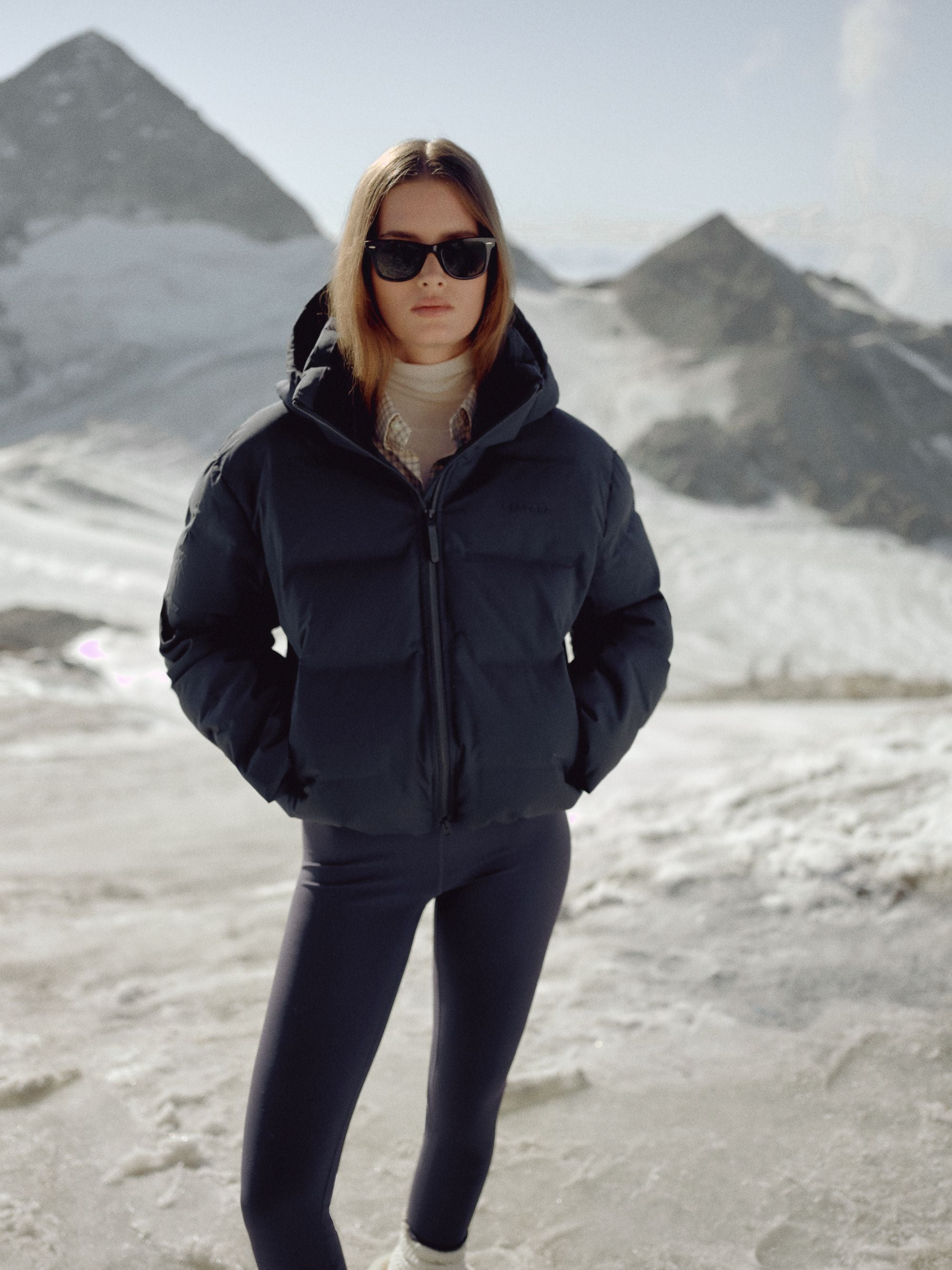 Woman wearing a navy CASPARA Aurora puffer jacket in a snowy mountain landscape.