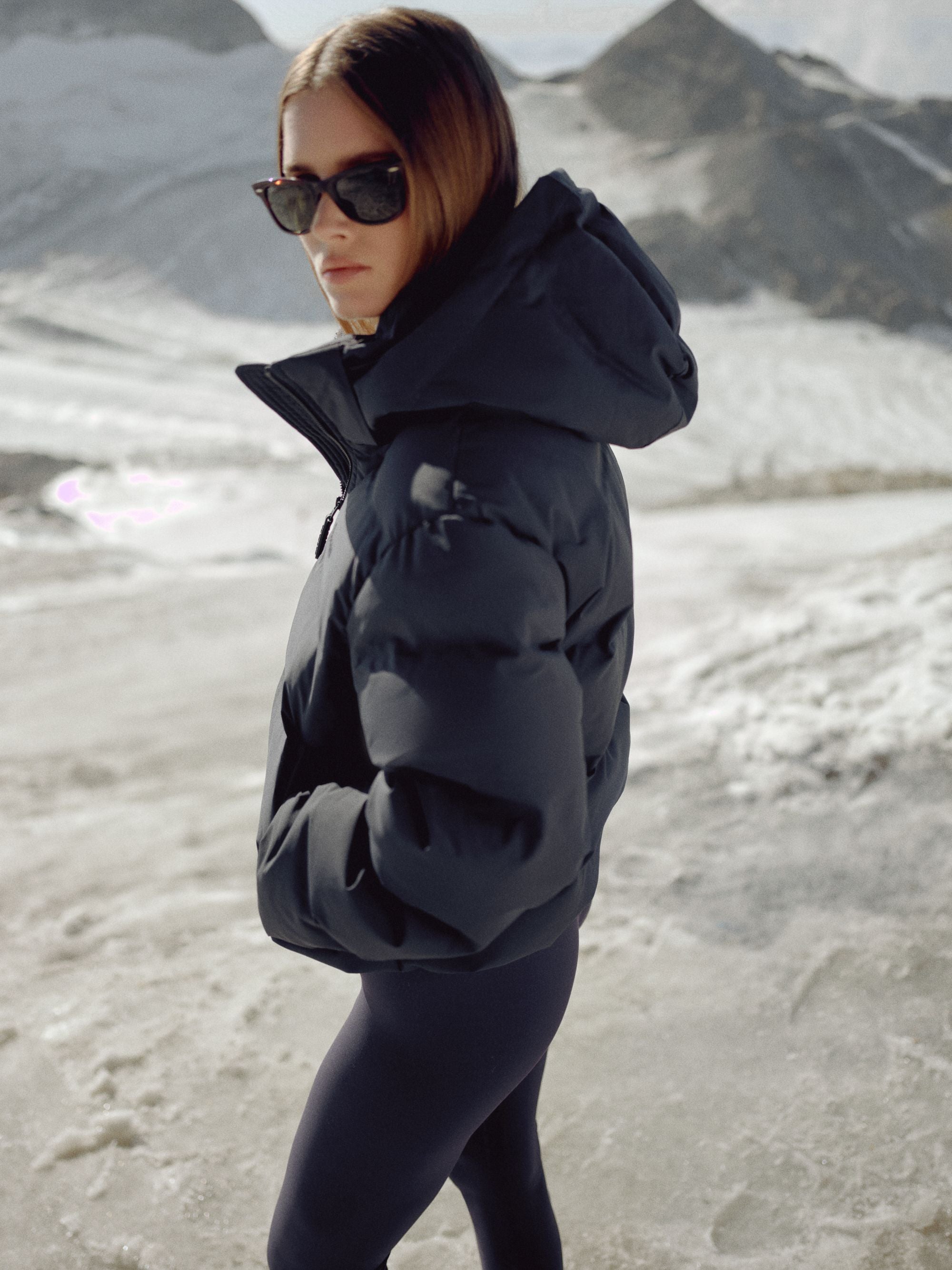 Woman wearing a navy CASPARA Aurora puffer jacket in a snowy mountain landscape.