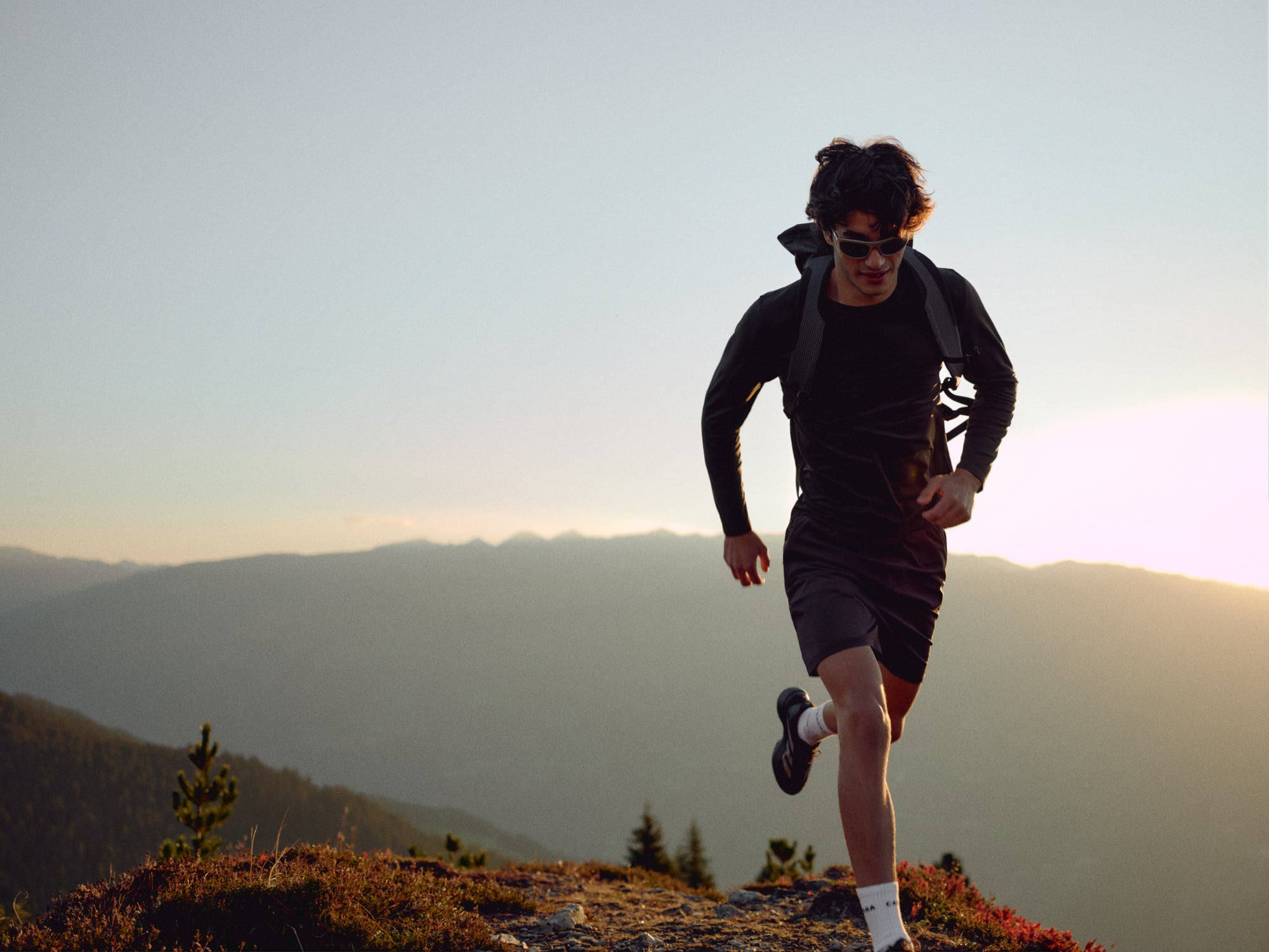 Man wearing espresso CASPARA Vantage 2-In-1 shorts trail running on a mountain ridge.
