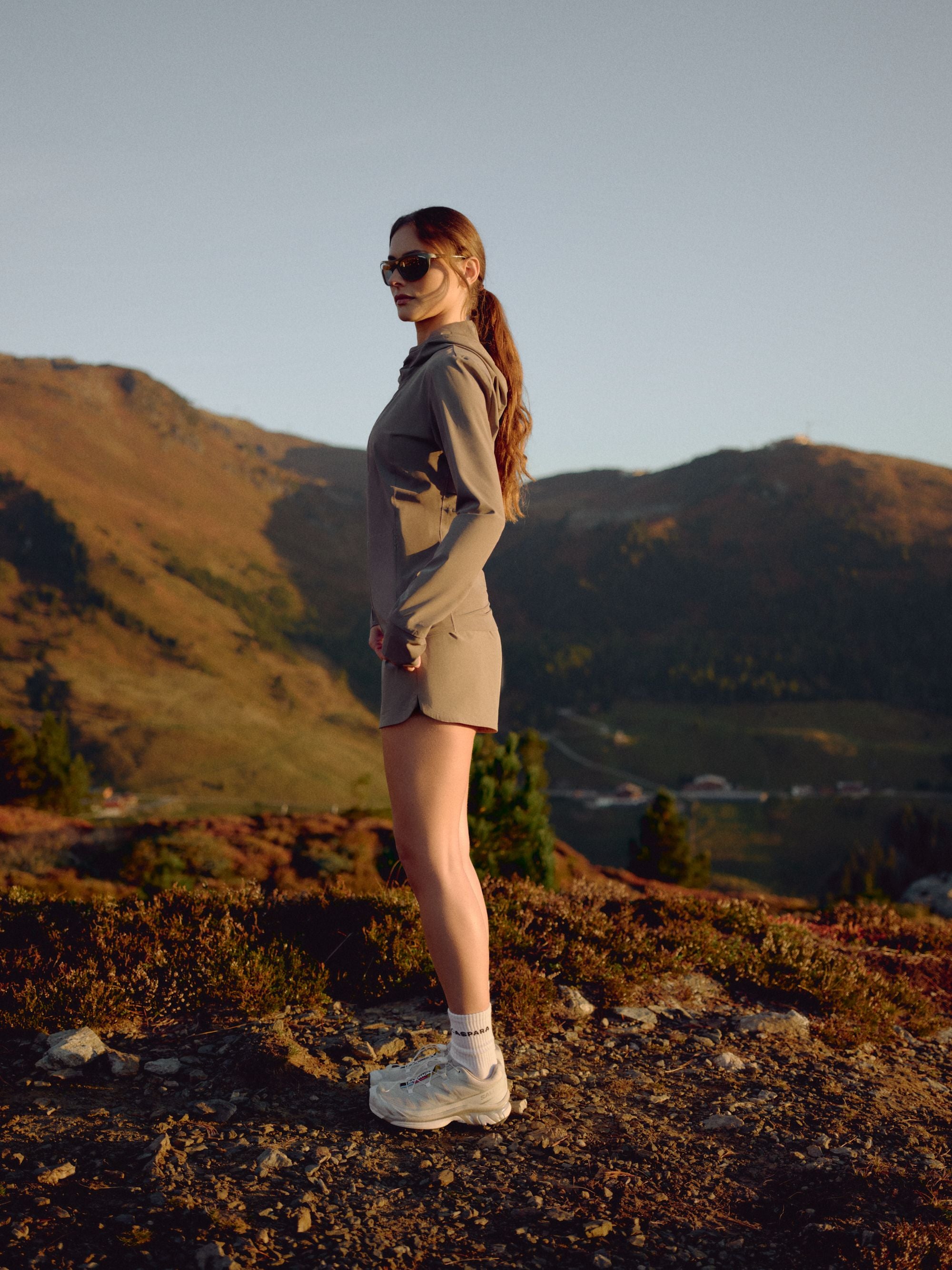 Woman wearing khaki CASPARA Aerluxe shorts standing on a mountain hillside.
