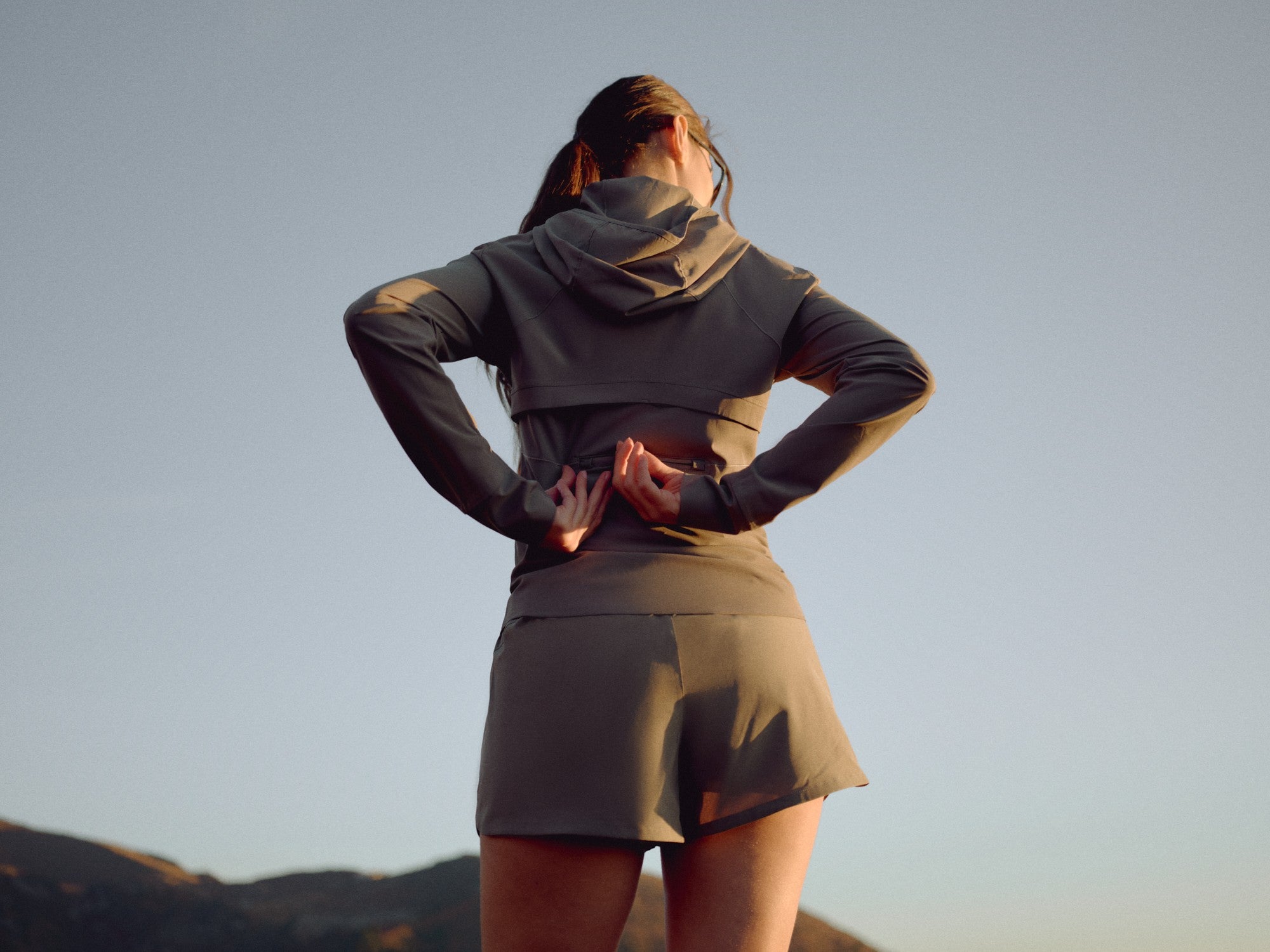 Back view of a woman wearing a khaki CASPARA Windluxe jacket outdoors.