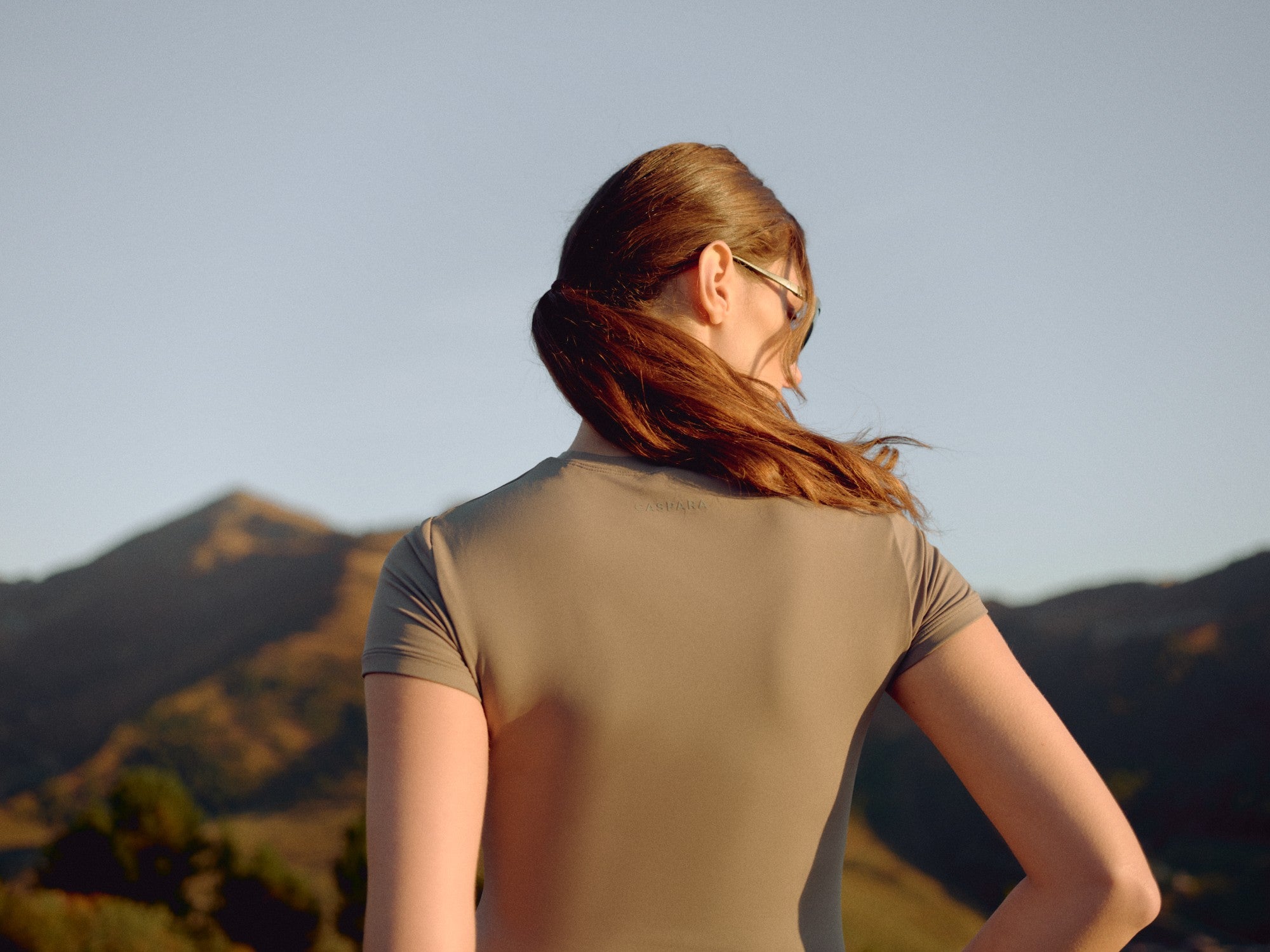 Woman wearing a khaki CASPARA Cloudform short sleeve top in a mountain landscape.