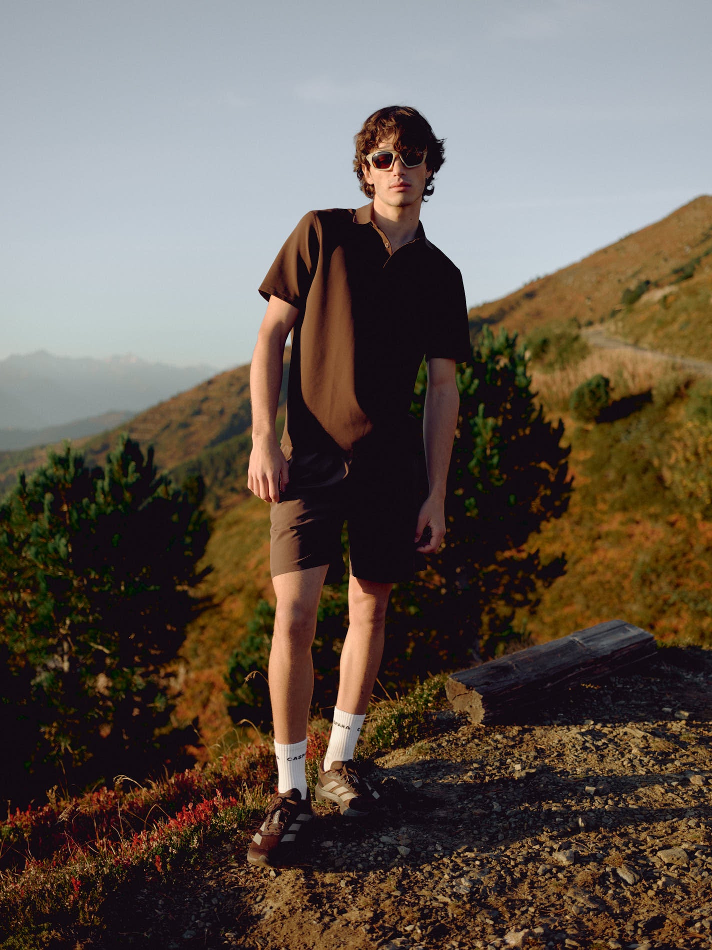Man wearing an espresso CASPARA Vantage polo tee standing on a mountain hillside.