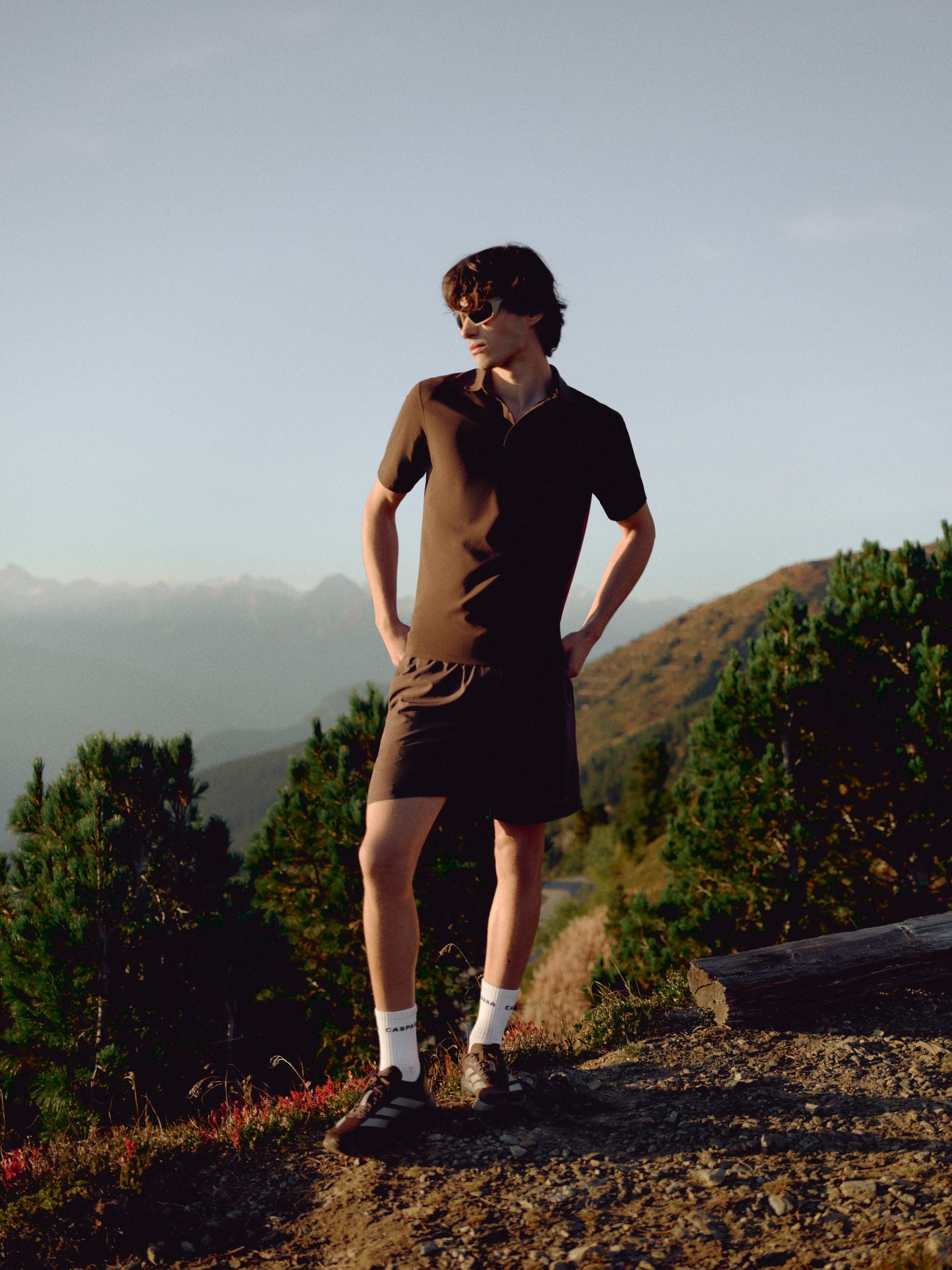 Man wearing an espresso CASPARA Vantage polo tee in a mountain landscape.