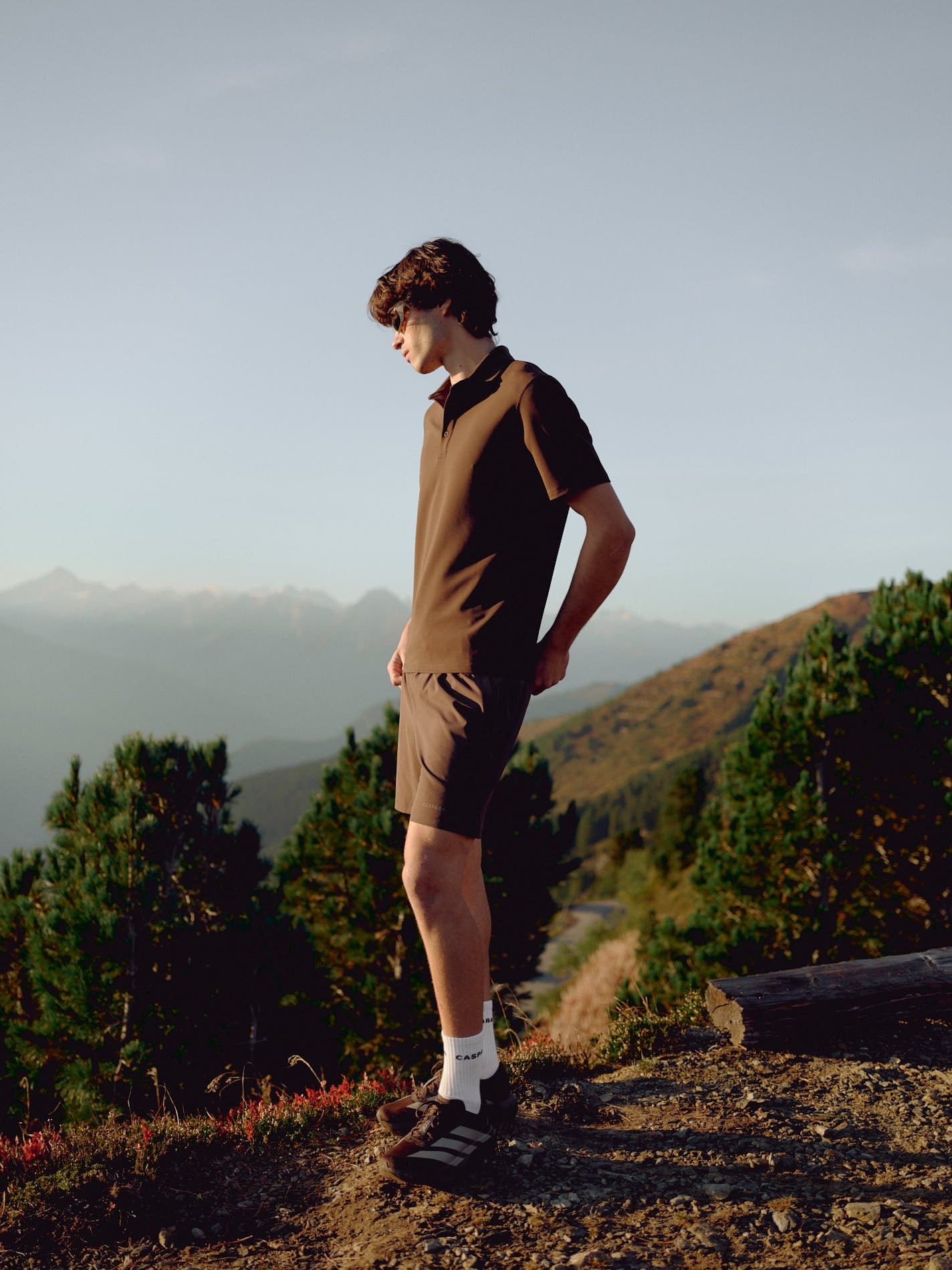 Man wearing an espresso CASPARA Vantage polo tee standing on a mountain hillside.