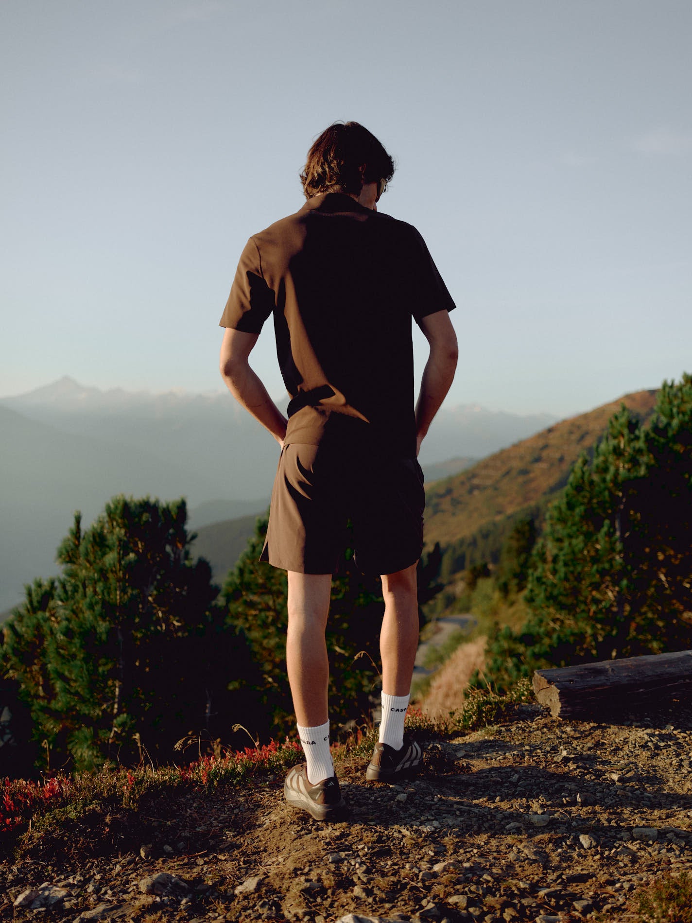 Rear view of a man wearing an espresso CASPARA Vantage polo tee in a mountain landscape.