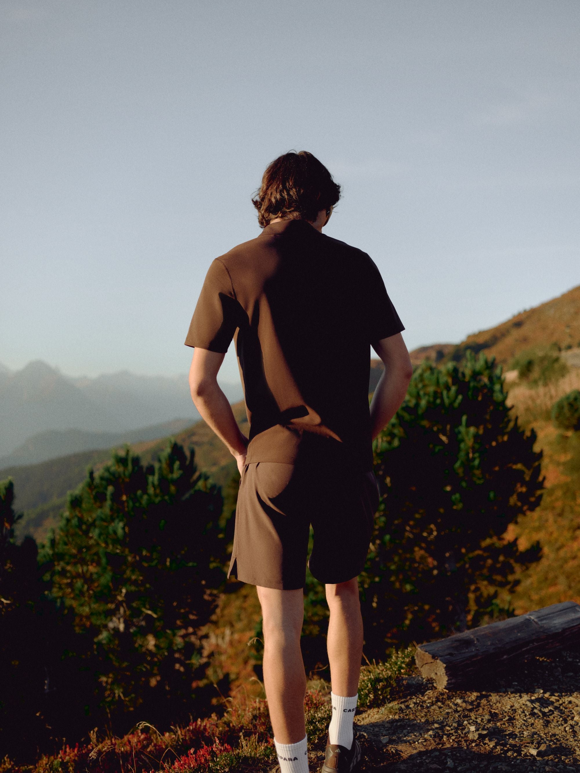 Man wearing an espresso CASPARA Vantage polo tee overlooking a mountain landscape.