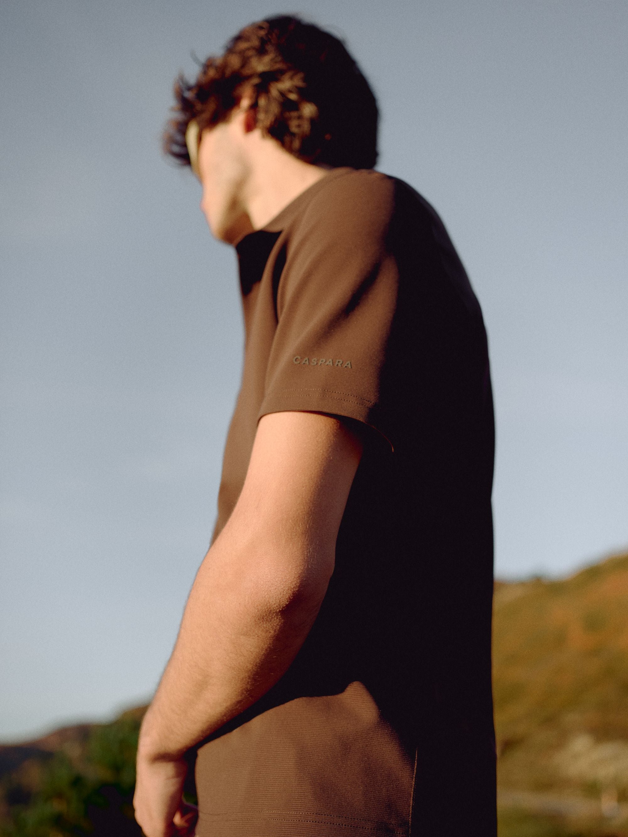 Man wearing an espresso CASPARA Vantage polo tee standing outdoors.