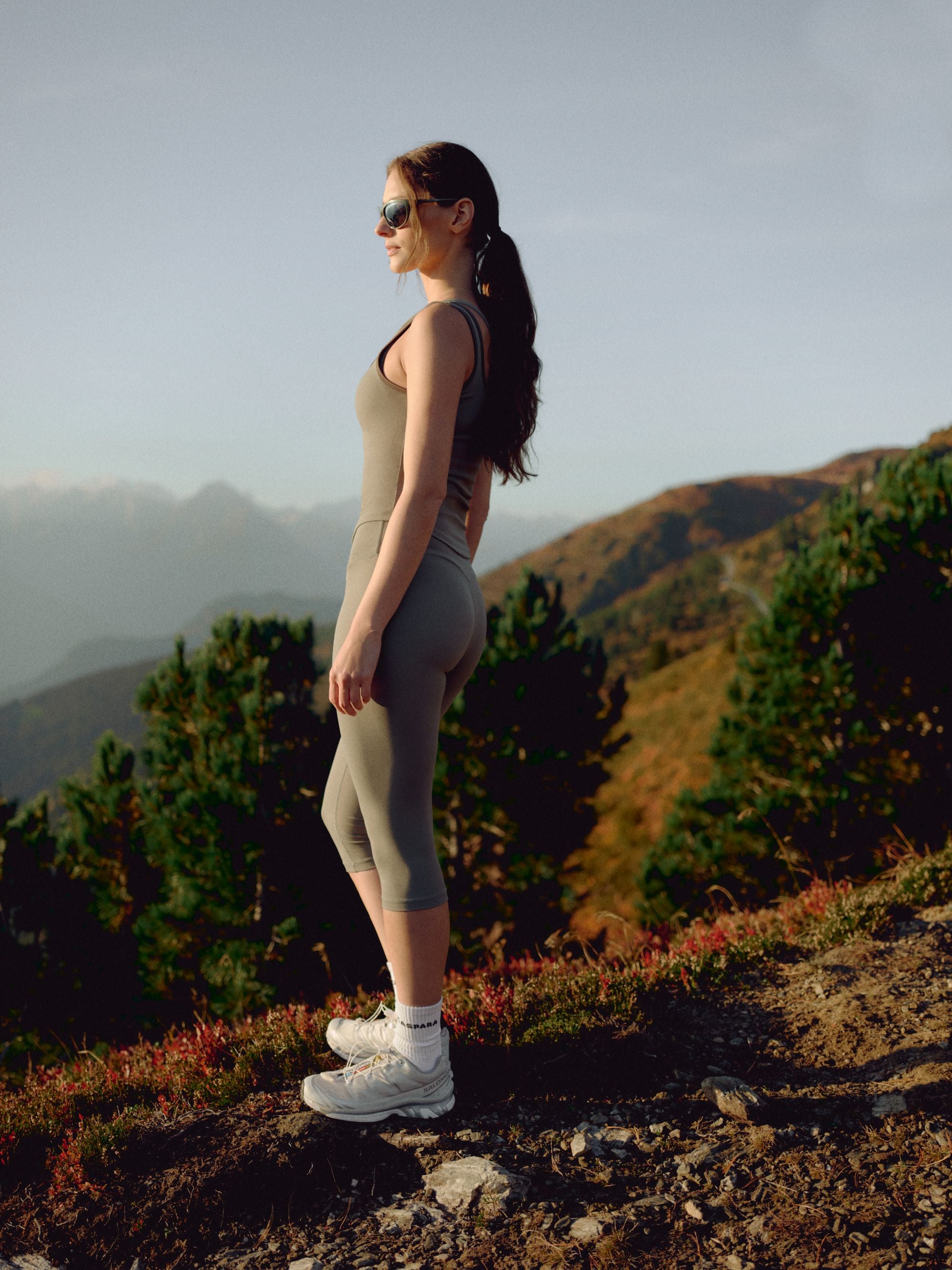 Woman wearing a khaki CASPARA Cloudform square neck top standing on a mountain hillside.