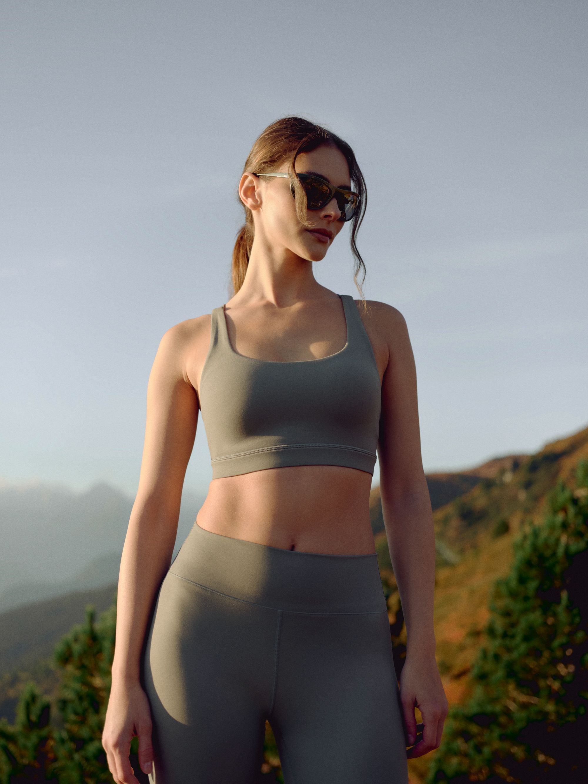 Woman wearing a khaki CASPARA Cloudform crossback sports bra in a mountain landscape.
