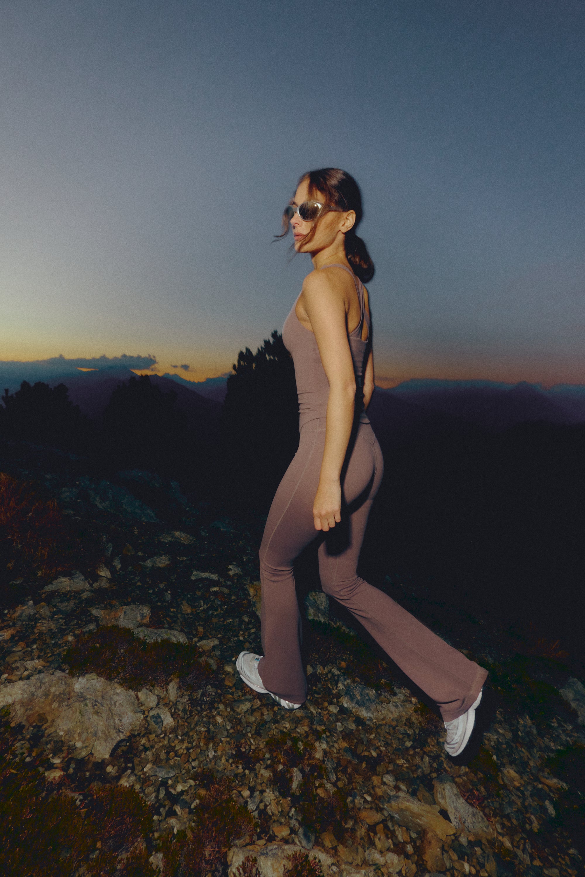 Woman wearing walnut CASPARA Cloudform yoga pants walking on a mountain trail at dusk.