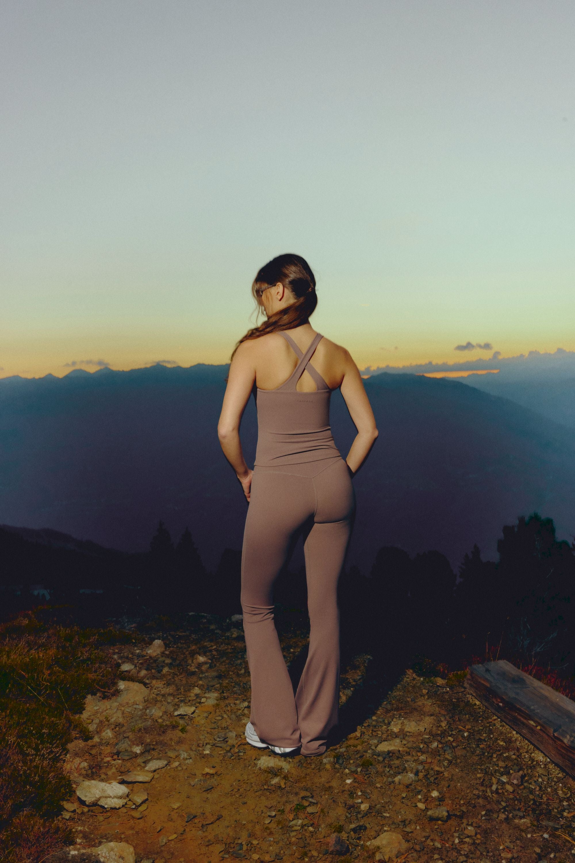 Woman wearing a walnut CASPARA Cloudform tank top and yoga pants in a mountain landscape.