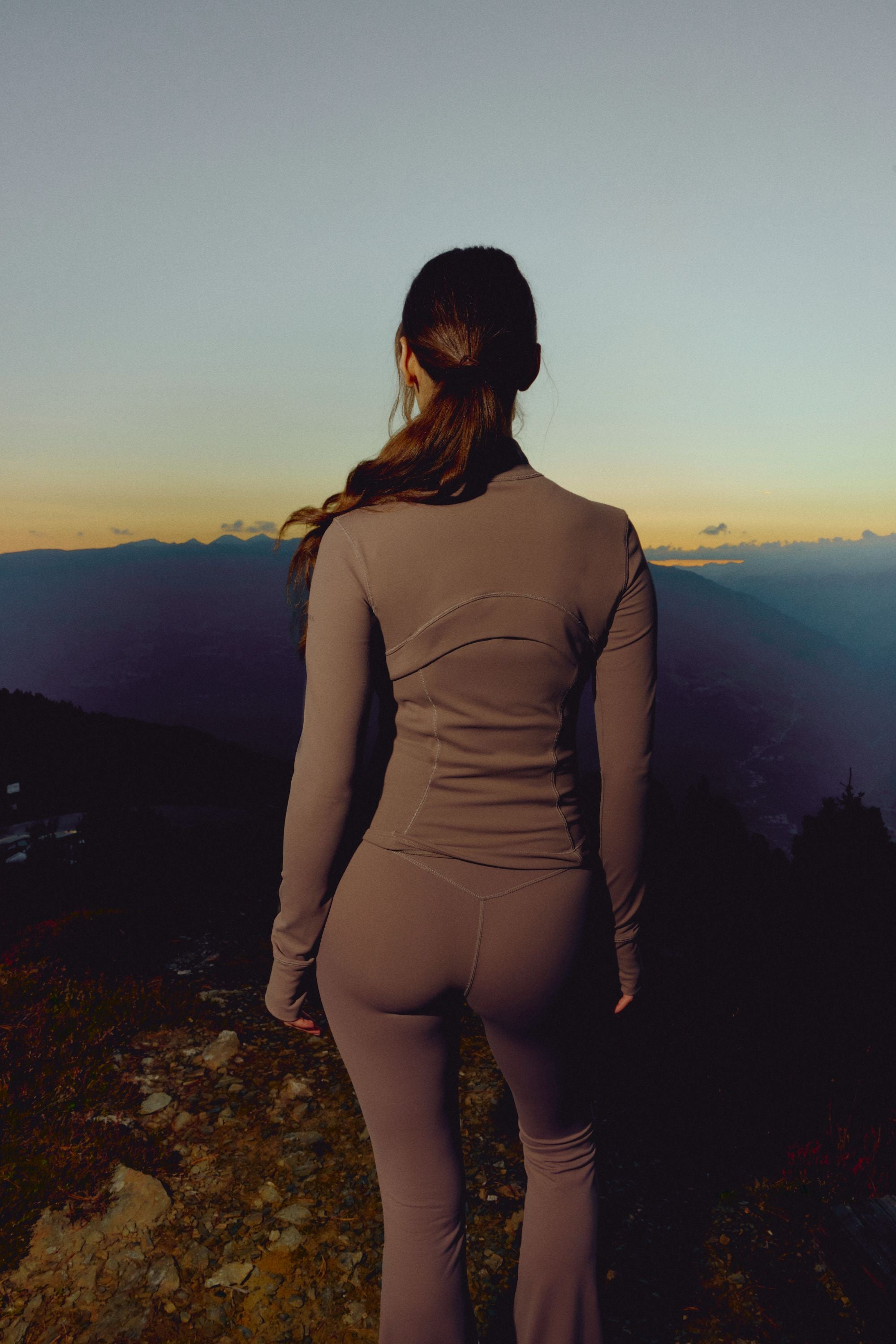 Woman wearing a walnut CASPARA Sculptluxe zip jacket overlooking mountains at sunset.