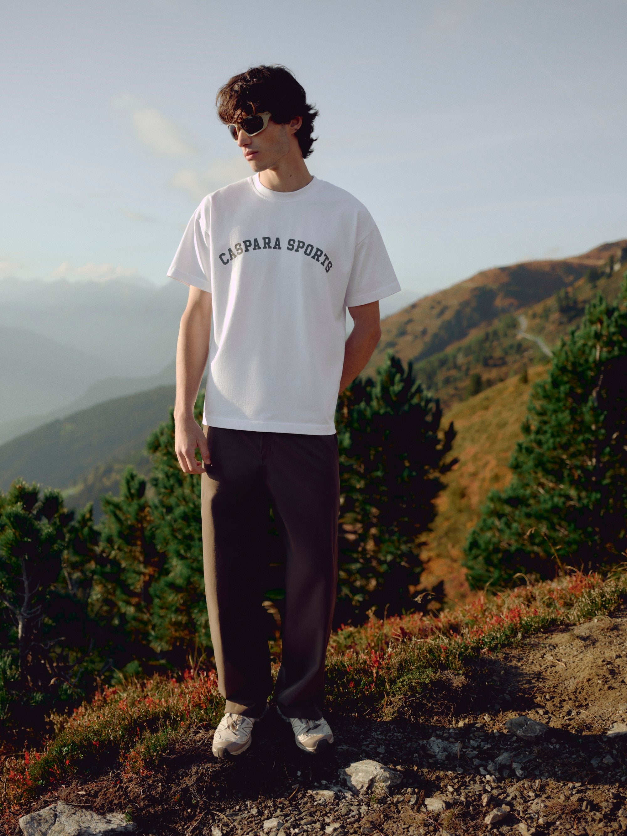 Man wearing a white CASPARA CS signature t-shirt in a mountain landscape.