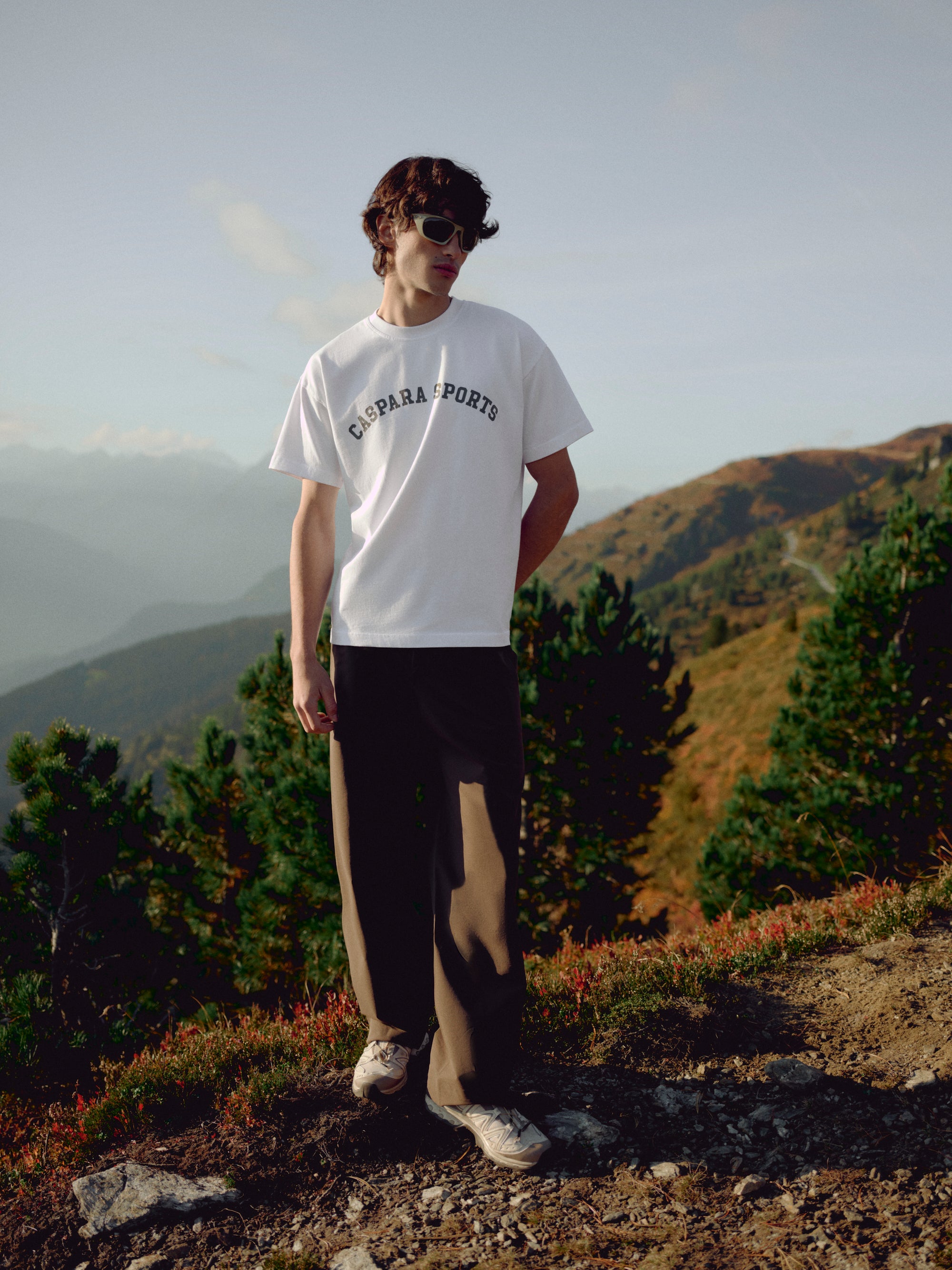 Man wearing a white CASPARA sports t-shirt standing on a mountain hillside.