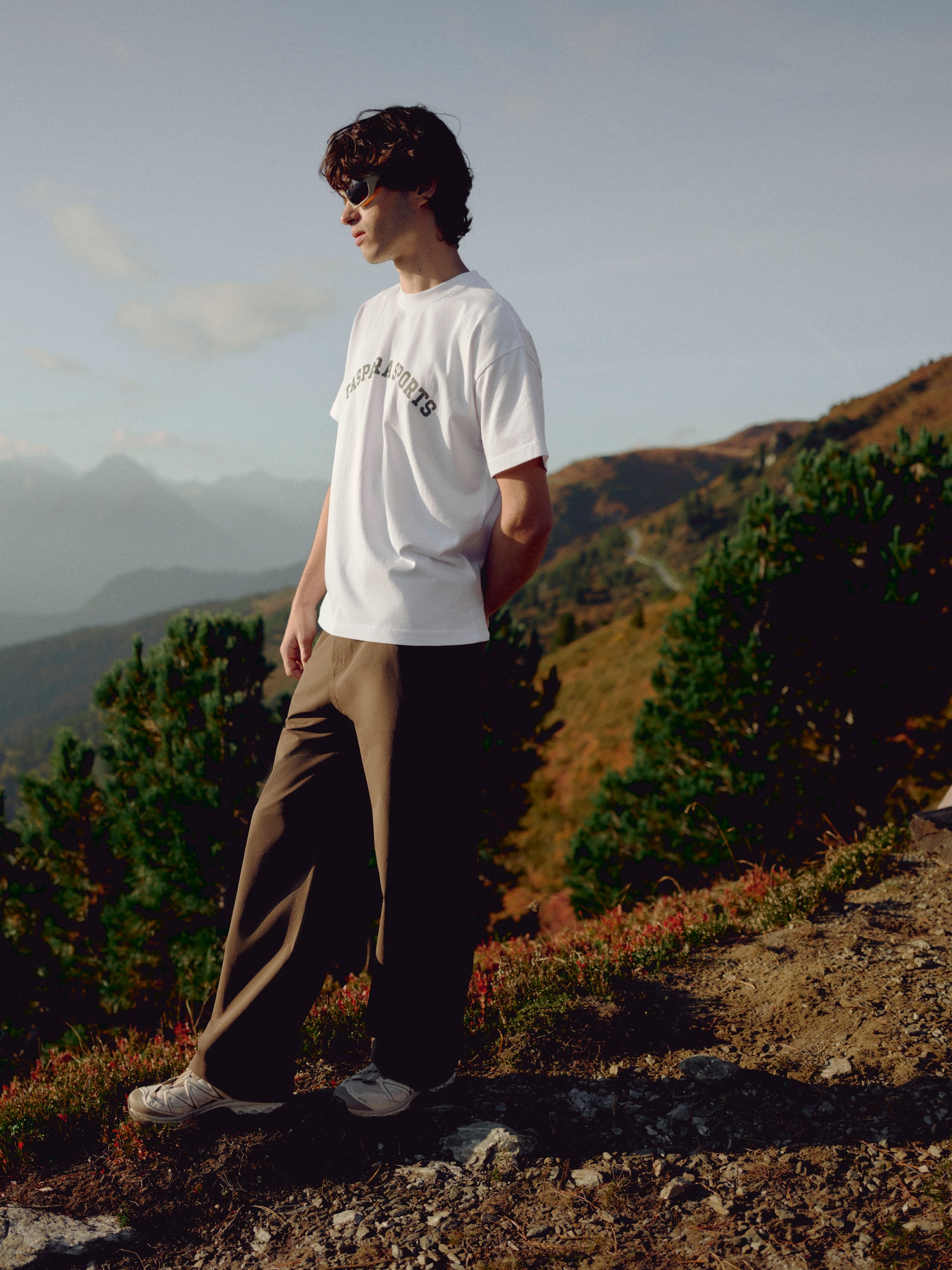 Man wearing a white CASPARA CS Signature tee standing on a mountain hillside.