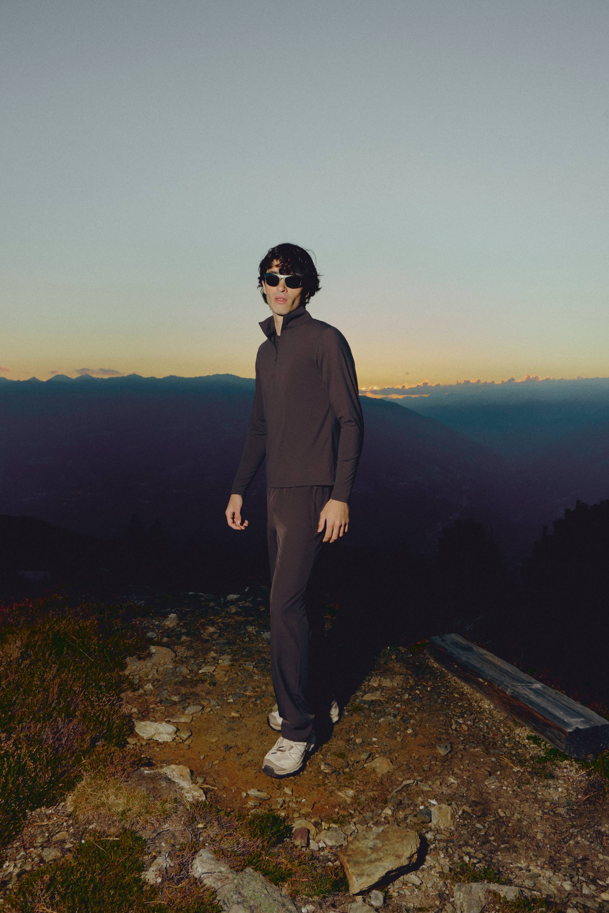 Man wearing an espresso CASPARA Prime Core half zip on a mountain trail at sunset.