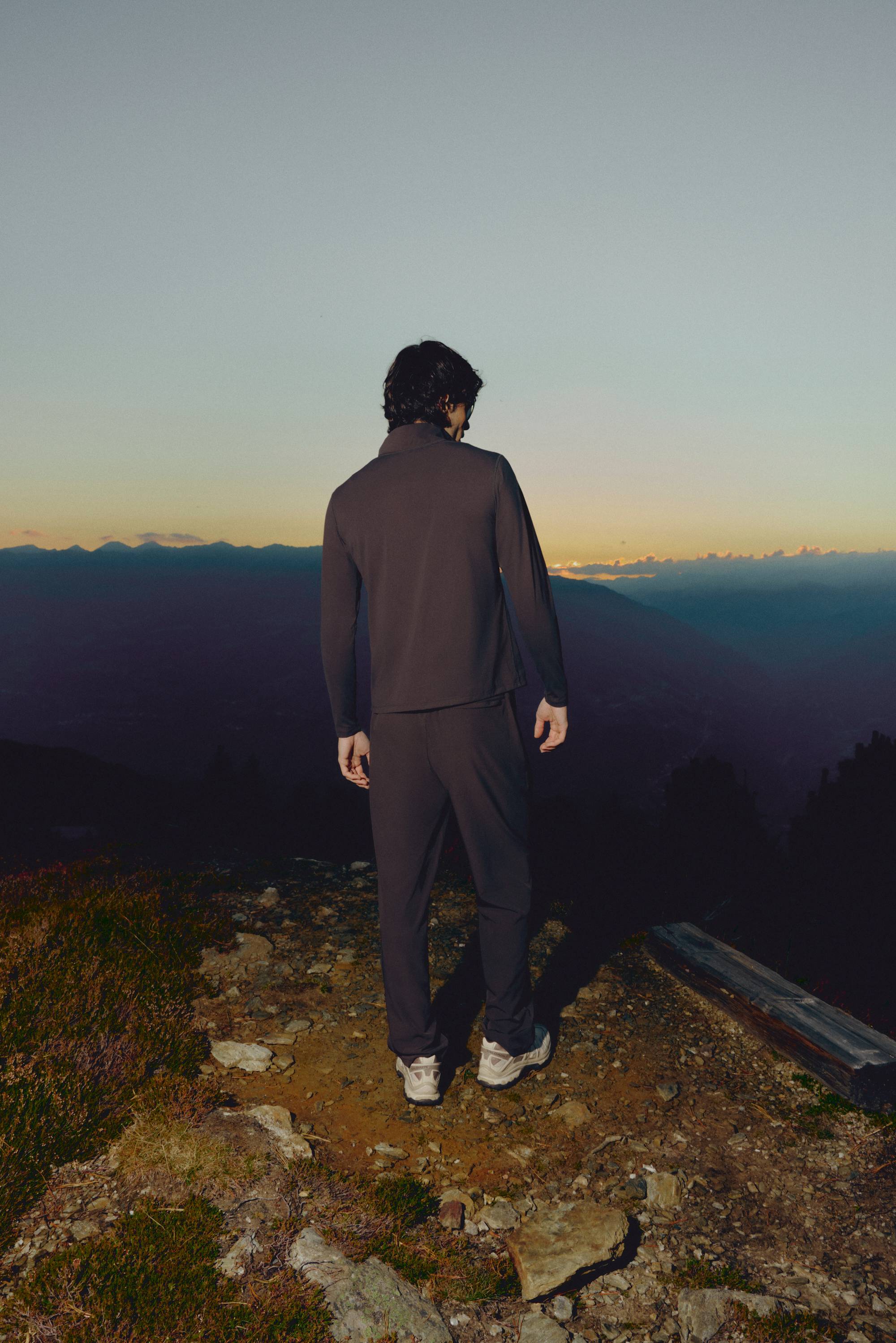 Man wearing espresso CASPARA Prime Core pants overlooking a mountain landscape at sunset.