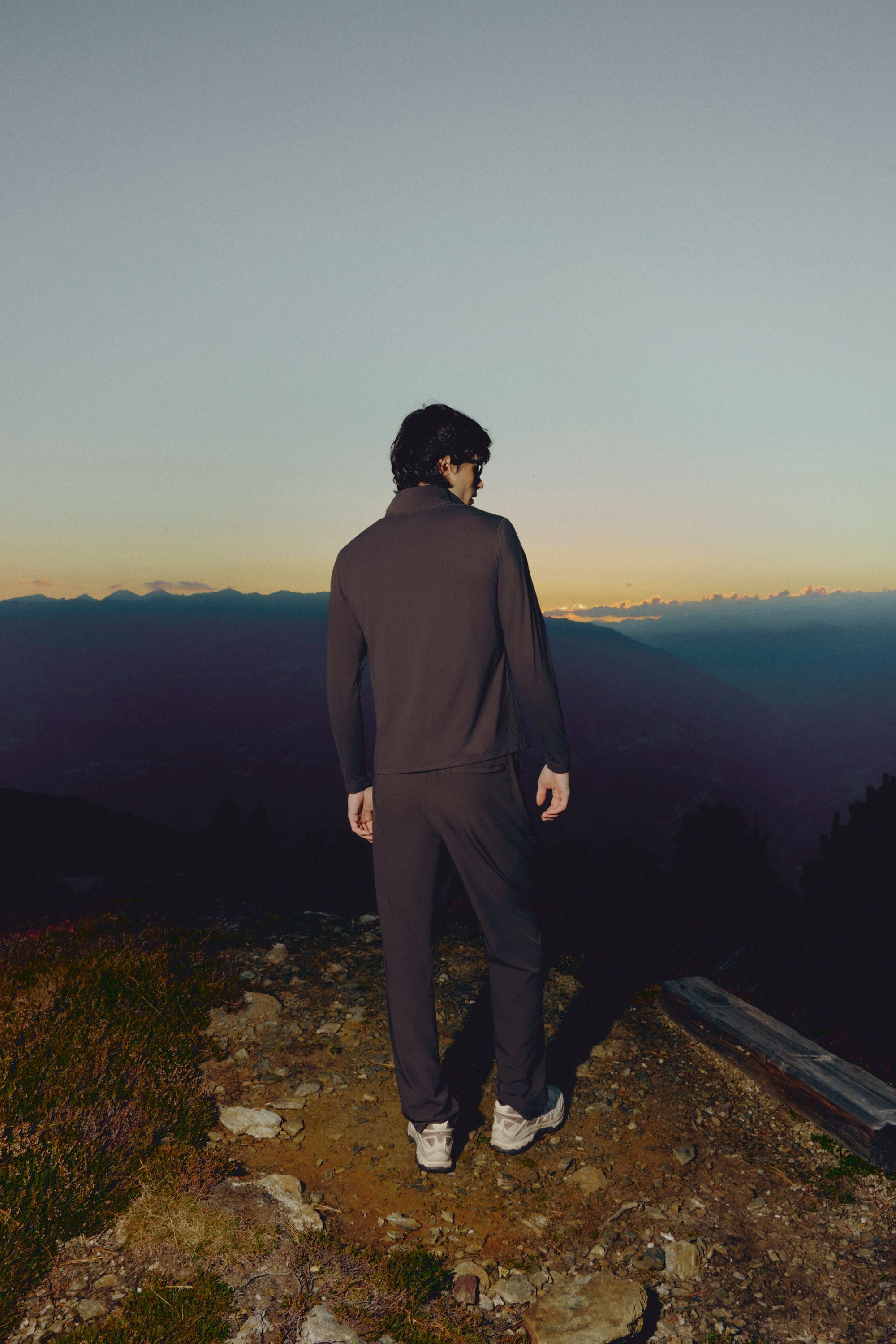 Man wearing an espresso CASPARA Prime Core half zip and pants overlooking mountains.