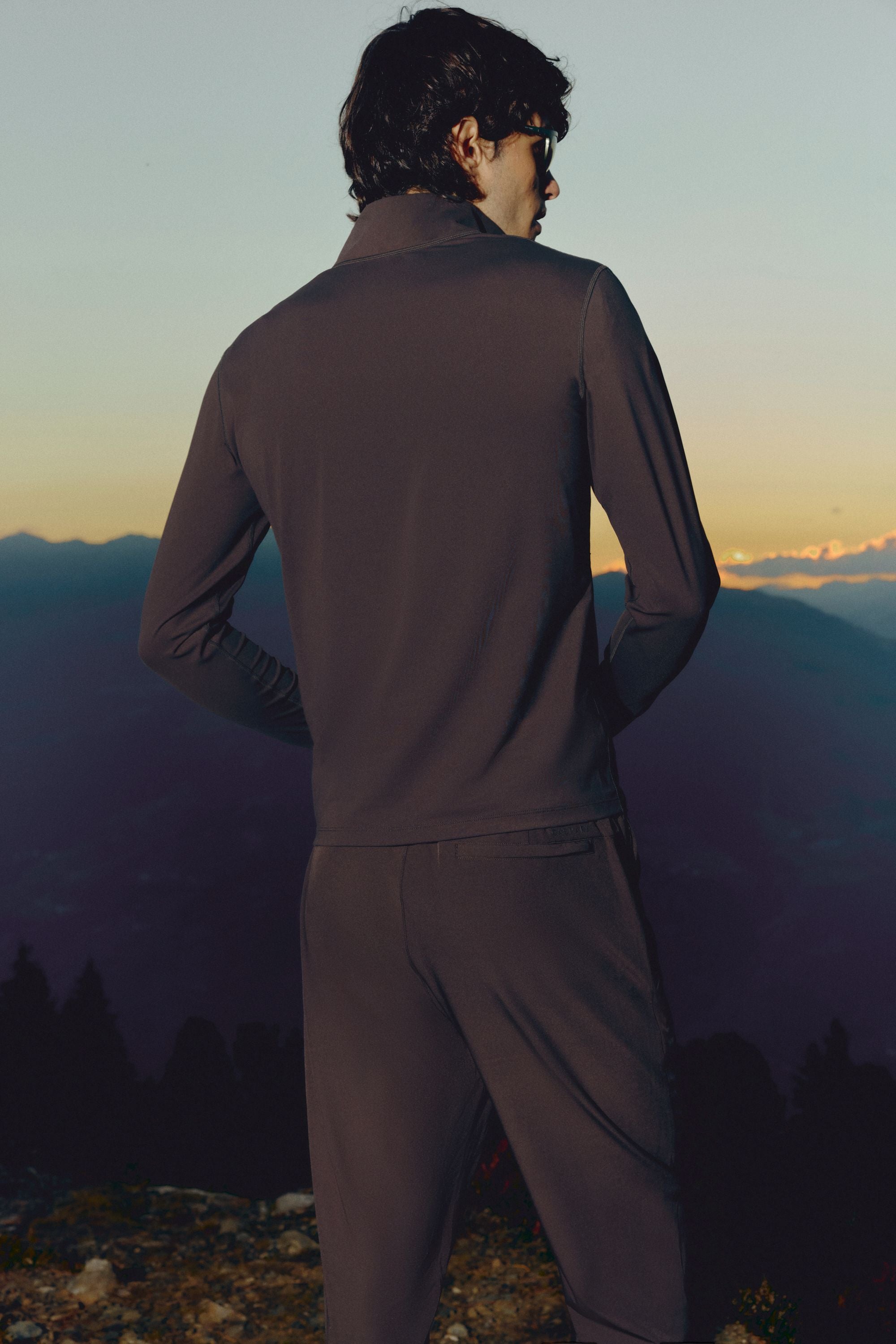 Back view of a man wearing an espresso CASPARA Prime Core half zip in a mountain landscape.