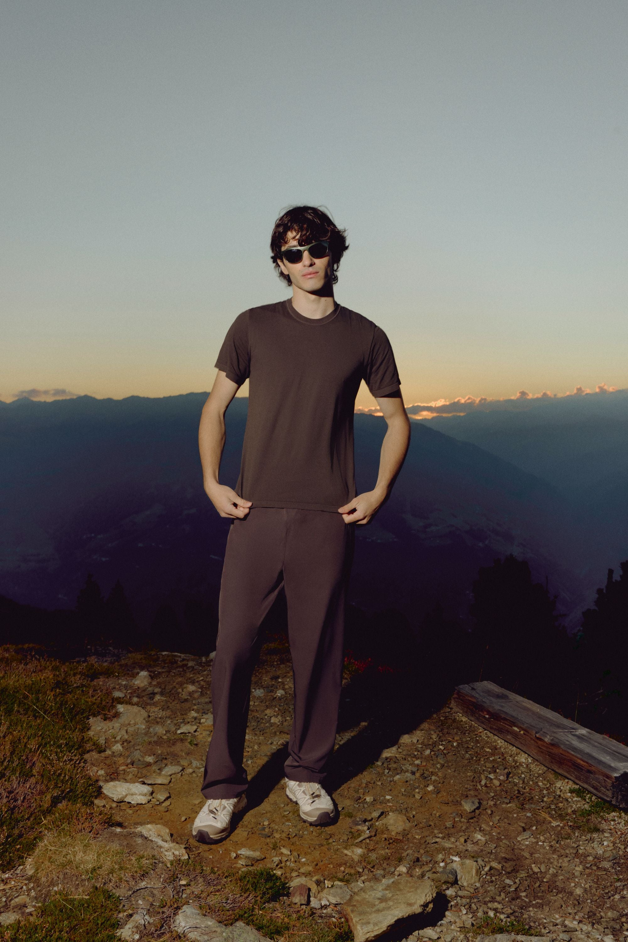 Man wearing an espresso CASPARA Seamlite tee standing on a mountain ridge.