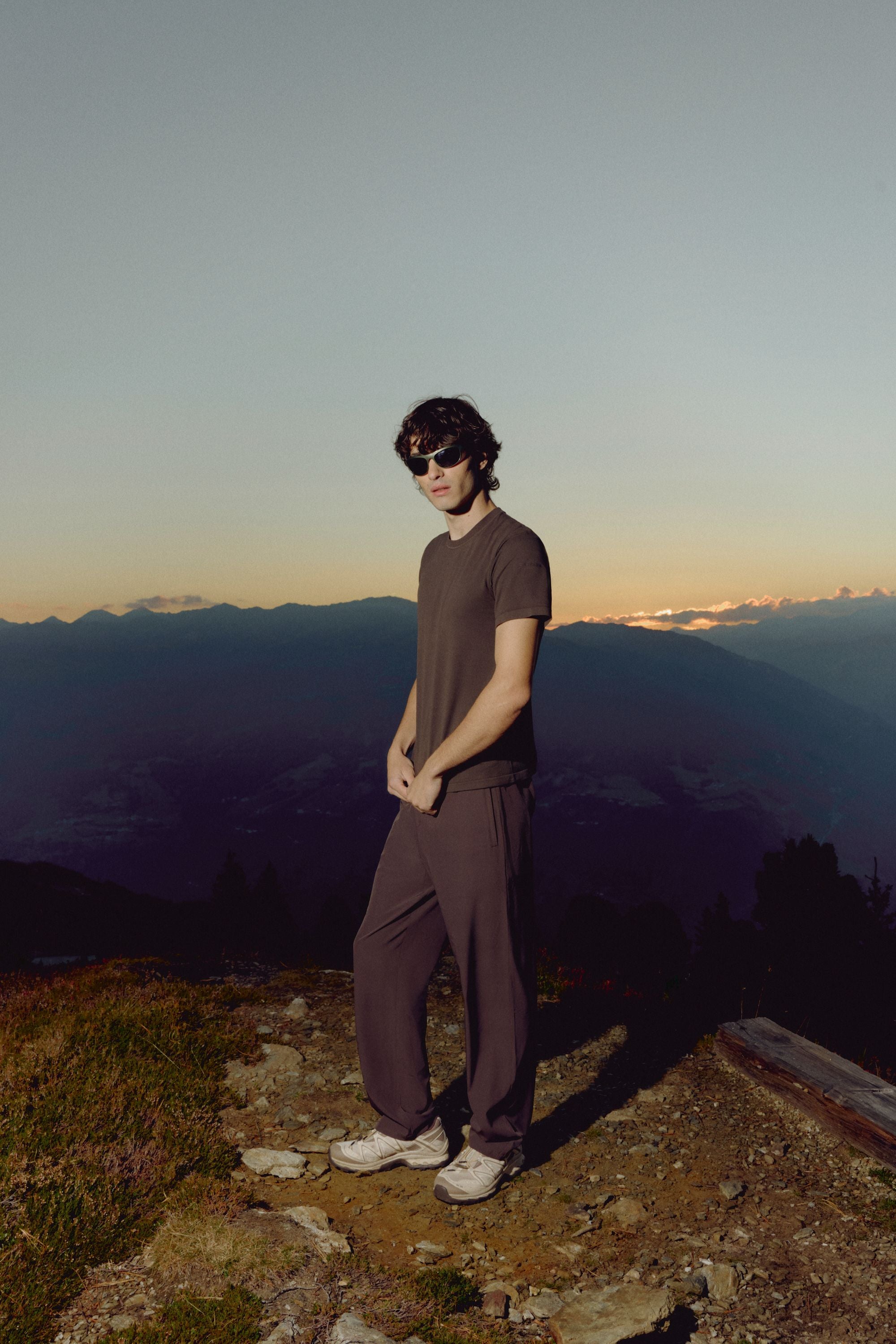 Man wearing an espresso CASPARA Seamlite tee standing on a mountain ridge at sunset.