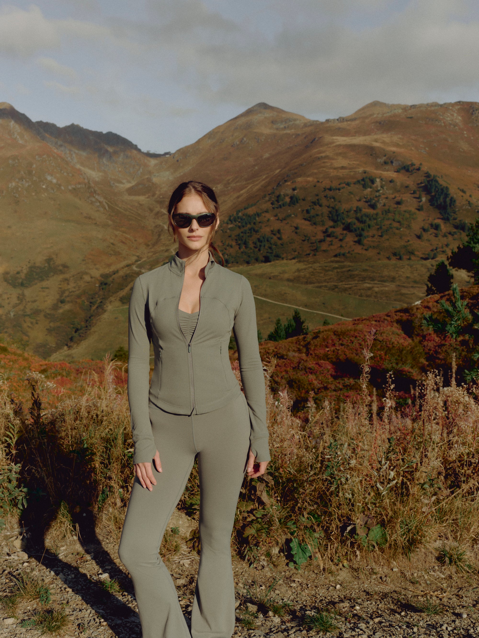 Woman wearing a khaki CASPARA Cloudform top and jacket in a mountain landscape.