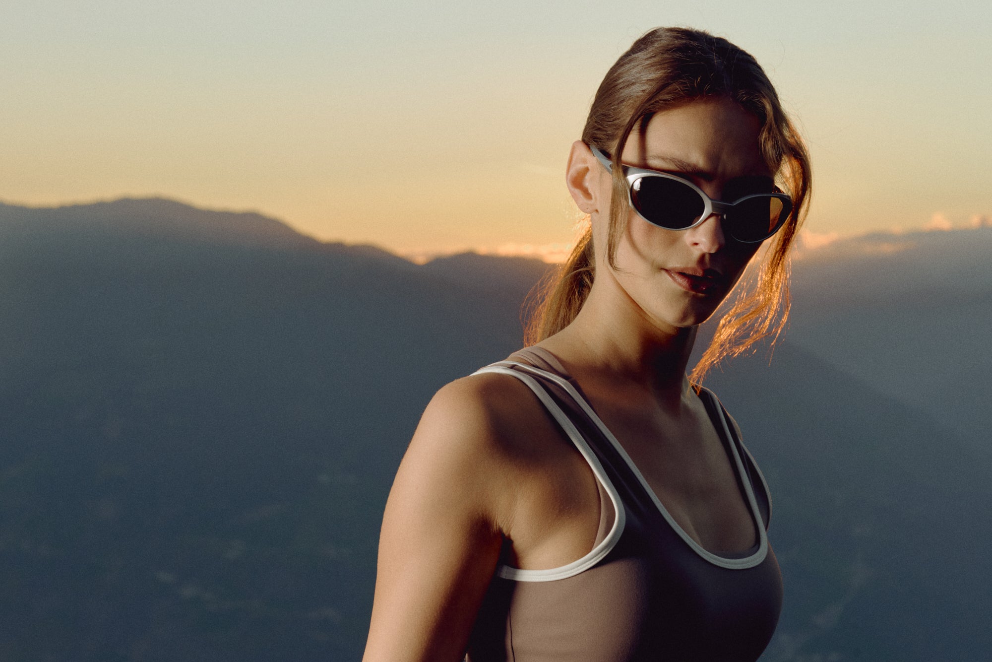 Woman wearing a walnut CASPARA Cloudform square neck top against a mountain sunset.
