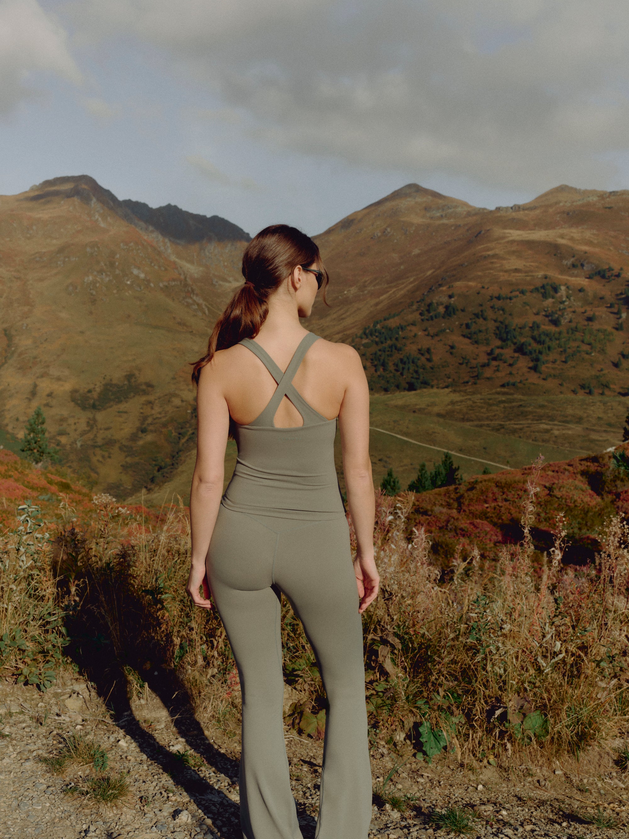 Woman wearing a khaki CASPARA Cloudform scrunch top with crossback straps in the mountains.