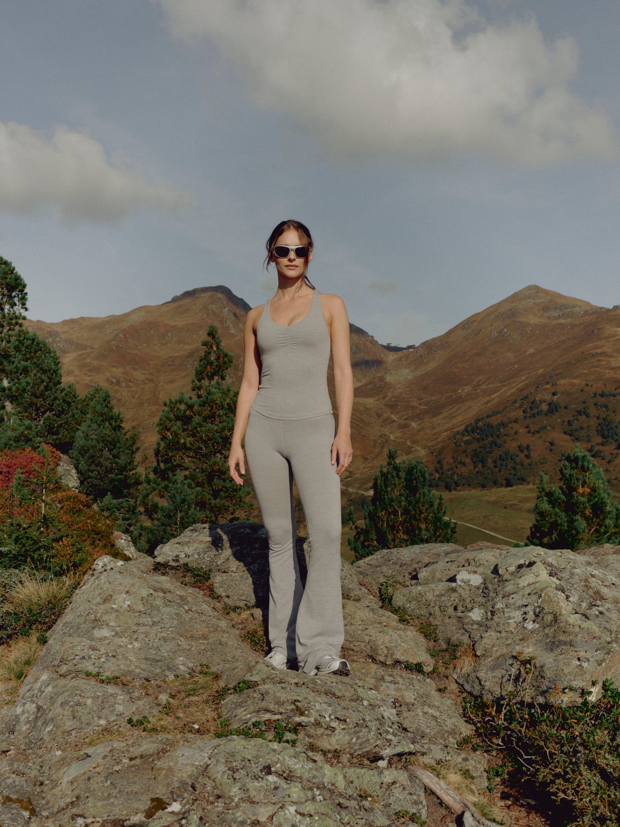 Woman wearing a grey melange CASPARA scrunch top and yoga pants in a mountain landscape.