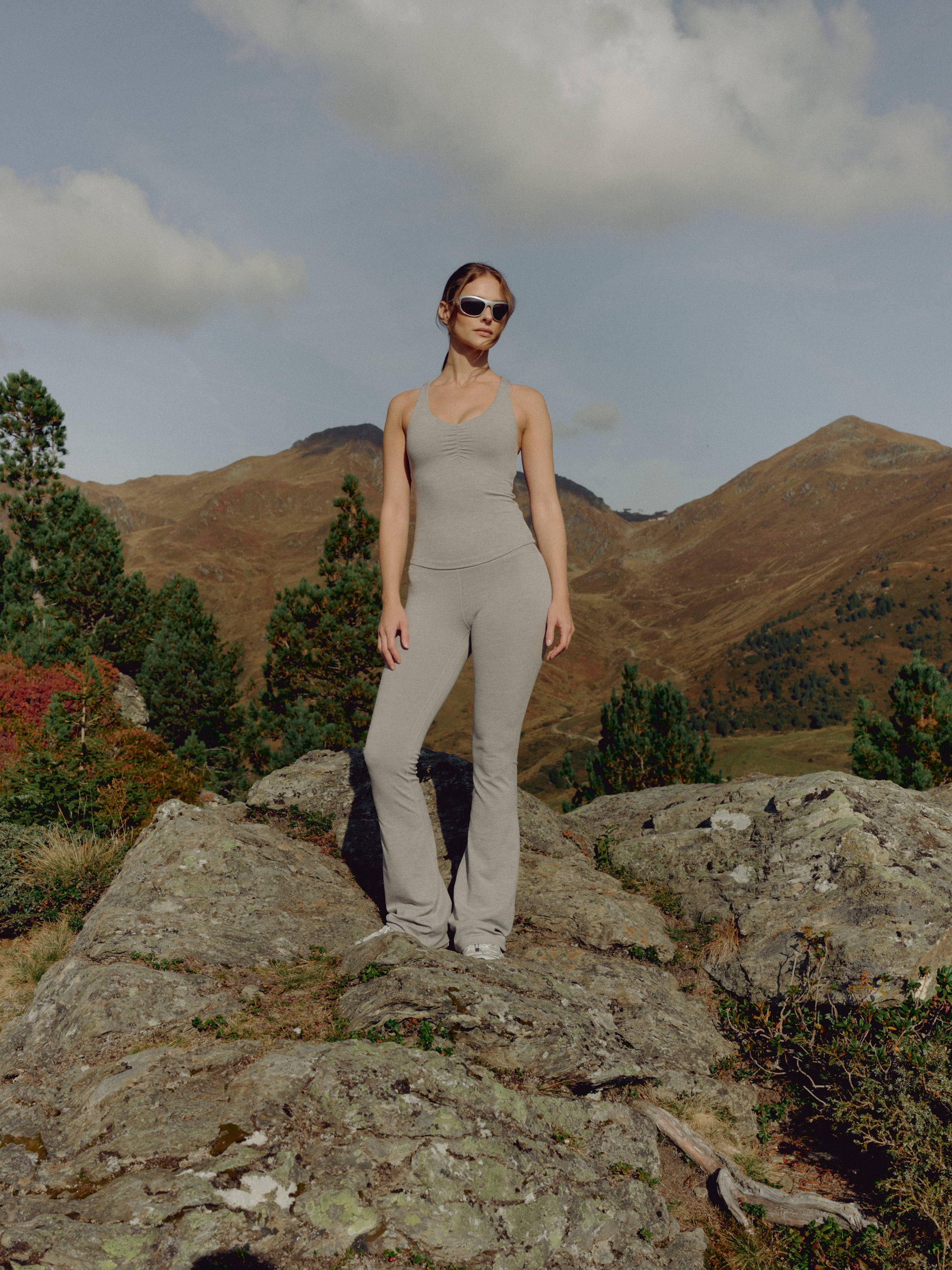 Woman wearing a grey melange CASPARA Cloudform top and yoga pants on a rocky hillside.