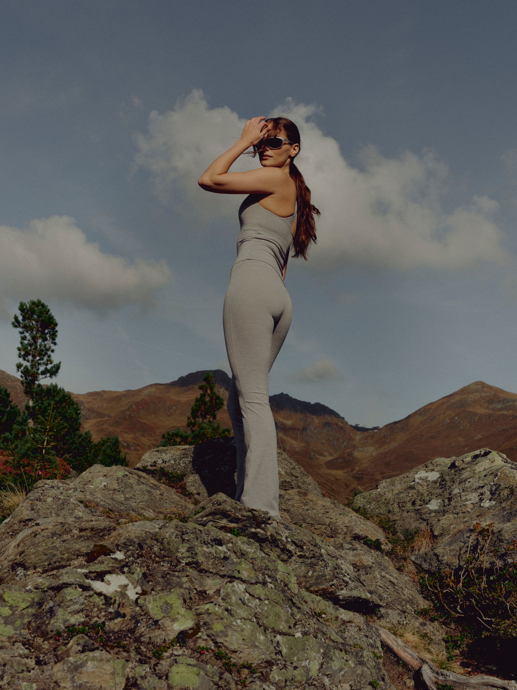 Woman wearing a grey melange CASPARA Cloudform top and yoga pants on a rocky hillside.