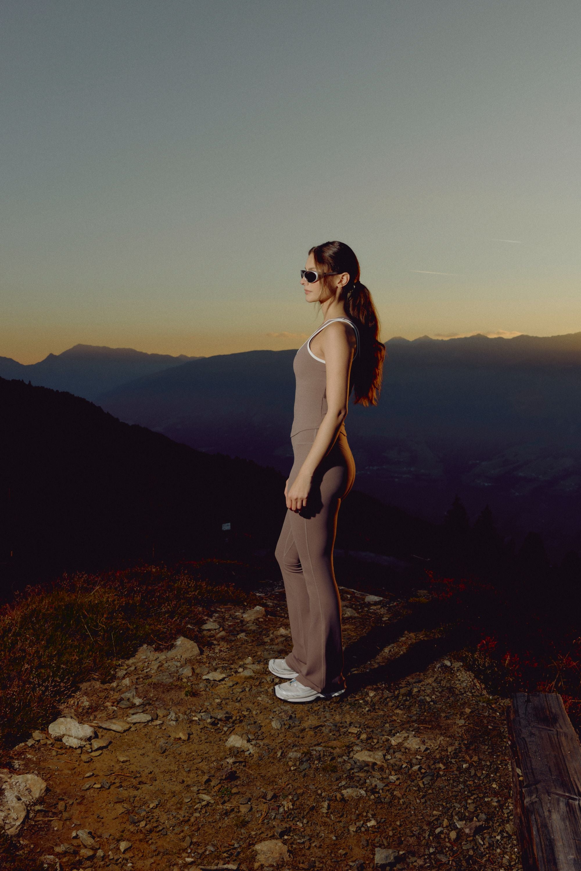 Woman wearing a walnut CASPARA Cloudform square neck top standing on a mountain ridge.